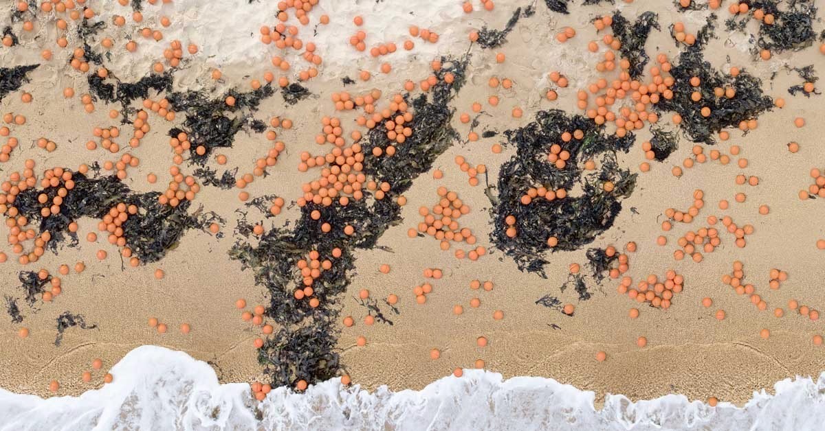 Aerial photo of an Australian beach with orange spheres scattered across the sand and seaweed, representing the marine debris source material.