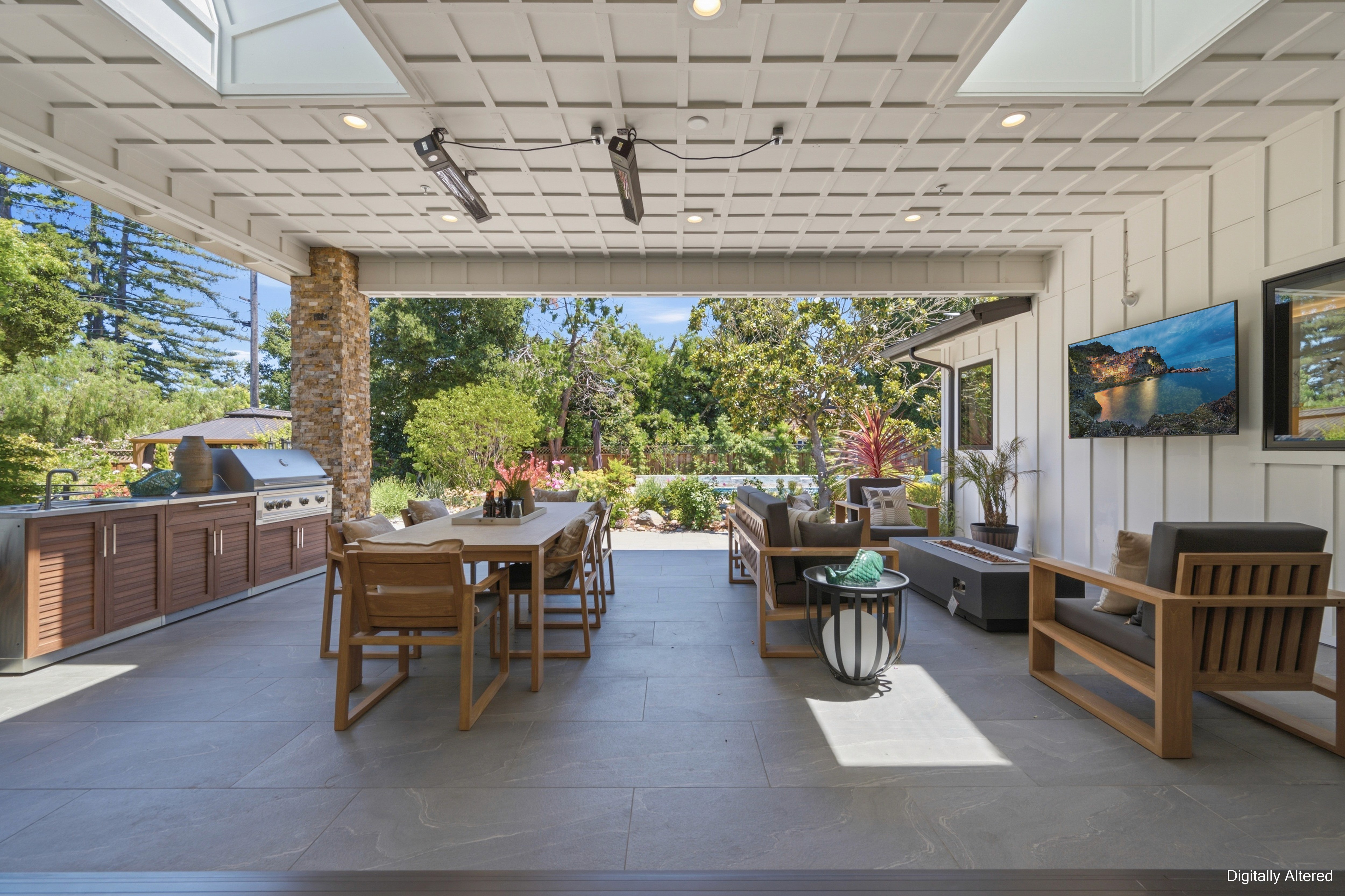 Covered patio with an outdoor dining table, built-in grill, wall-mounted TV, and views of the landscaped backyard.