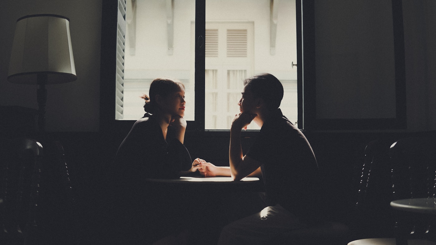 Two colleagues seated across a table in silhouette against a bright window