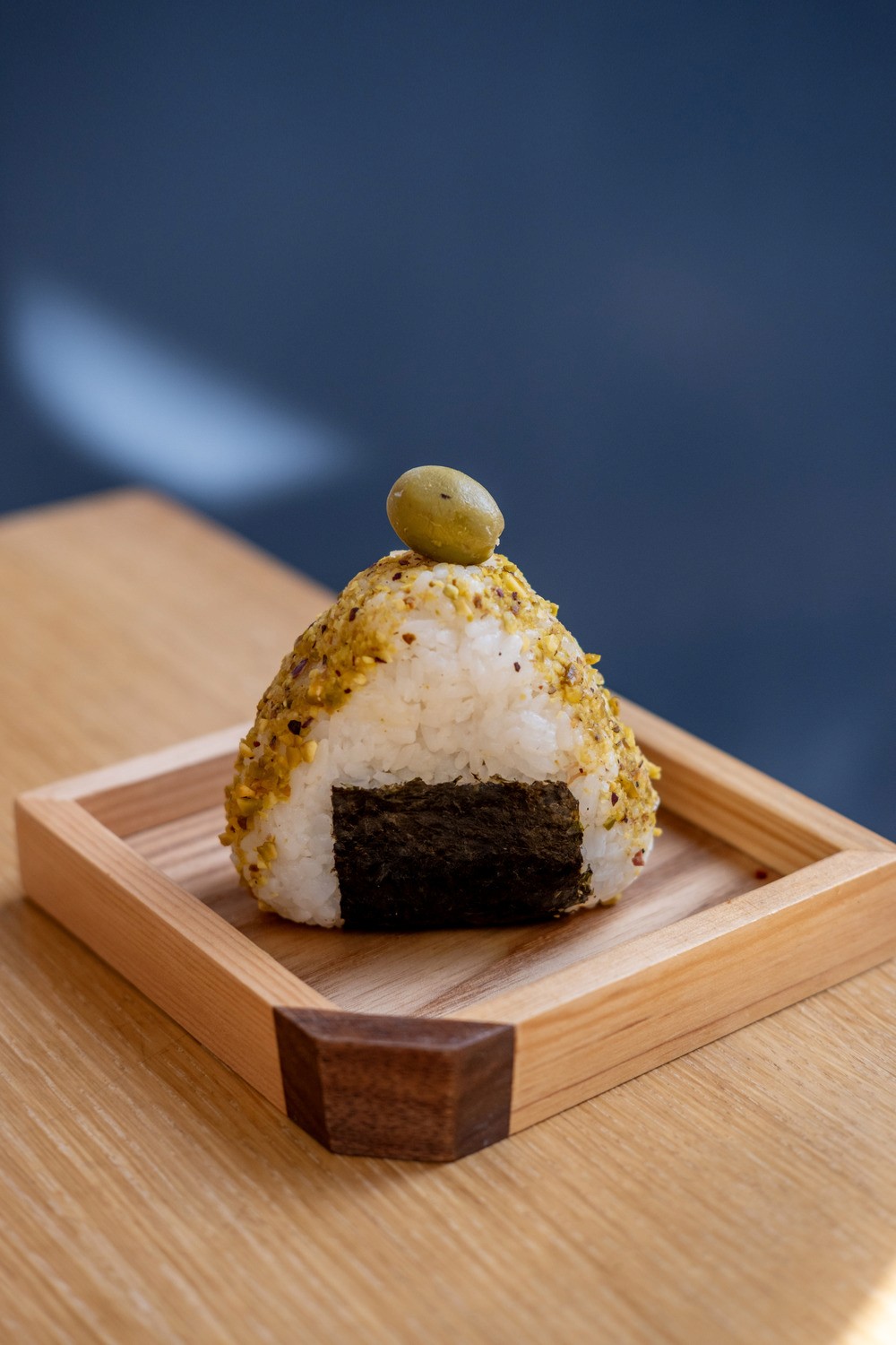 Person with a mustache wearing a black t-shirt carrying a tall stack of pizza boxes inside a dimly lit bar or restaurant.
