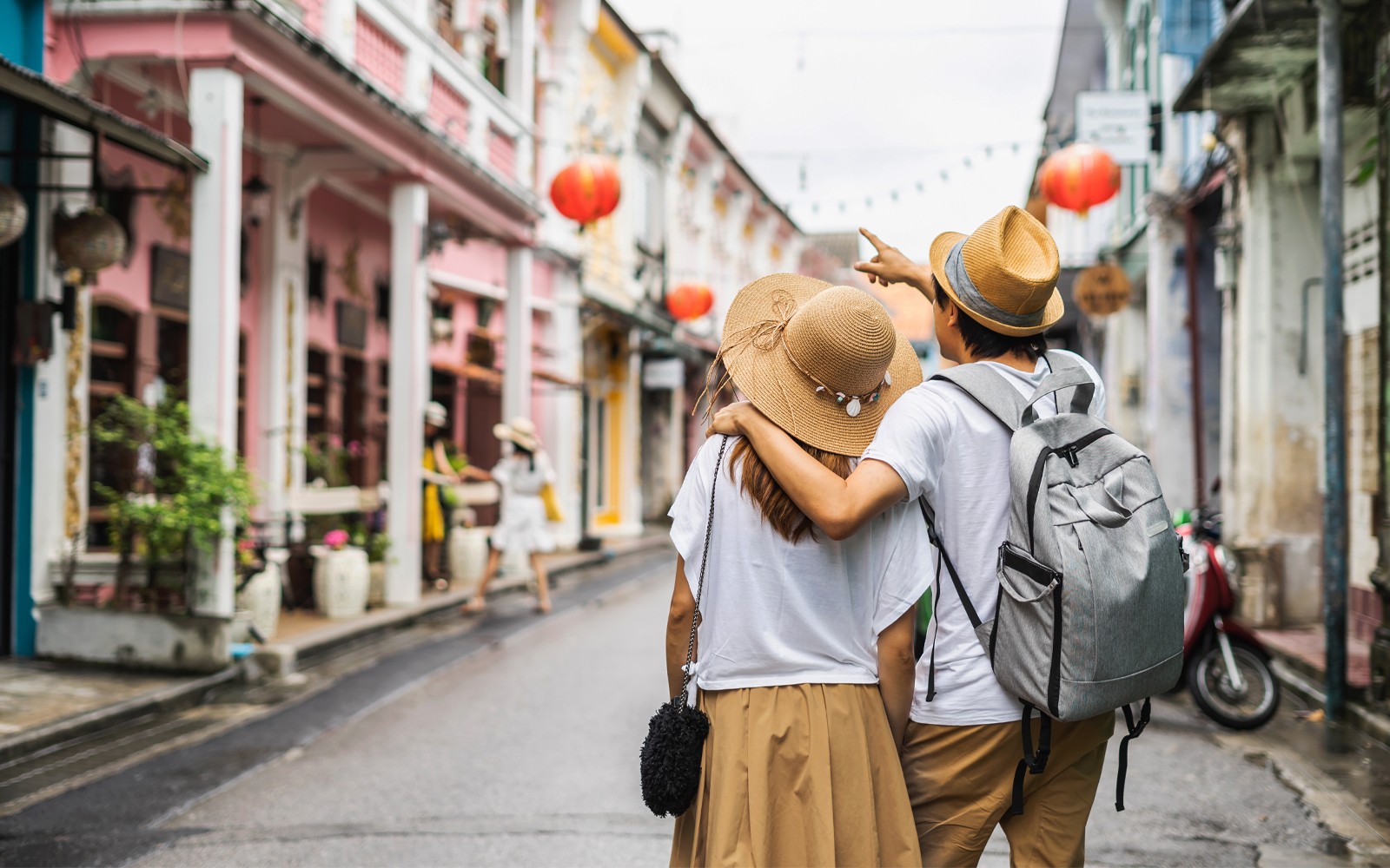 คู่รักวัยหนุ่มสาวเดินผ่านถนนเมืองเก่าที่เต็มไปด้วยร้านค้าและโคมแดง