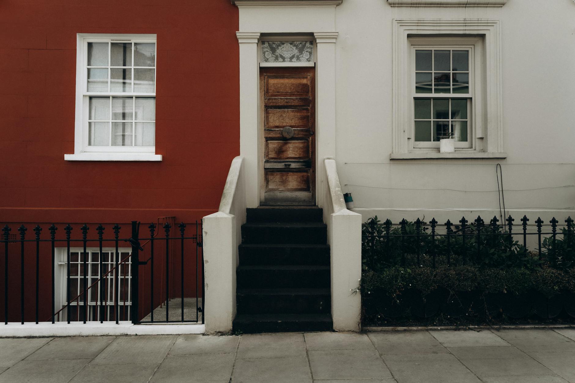 Adjoining red and cream London townhouses with a wooden front door, stone steps and black iron railings on the pavement.