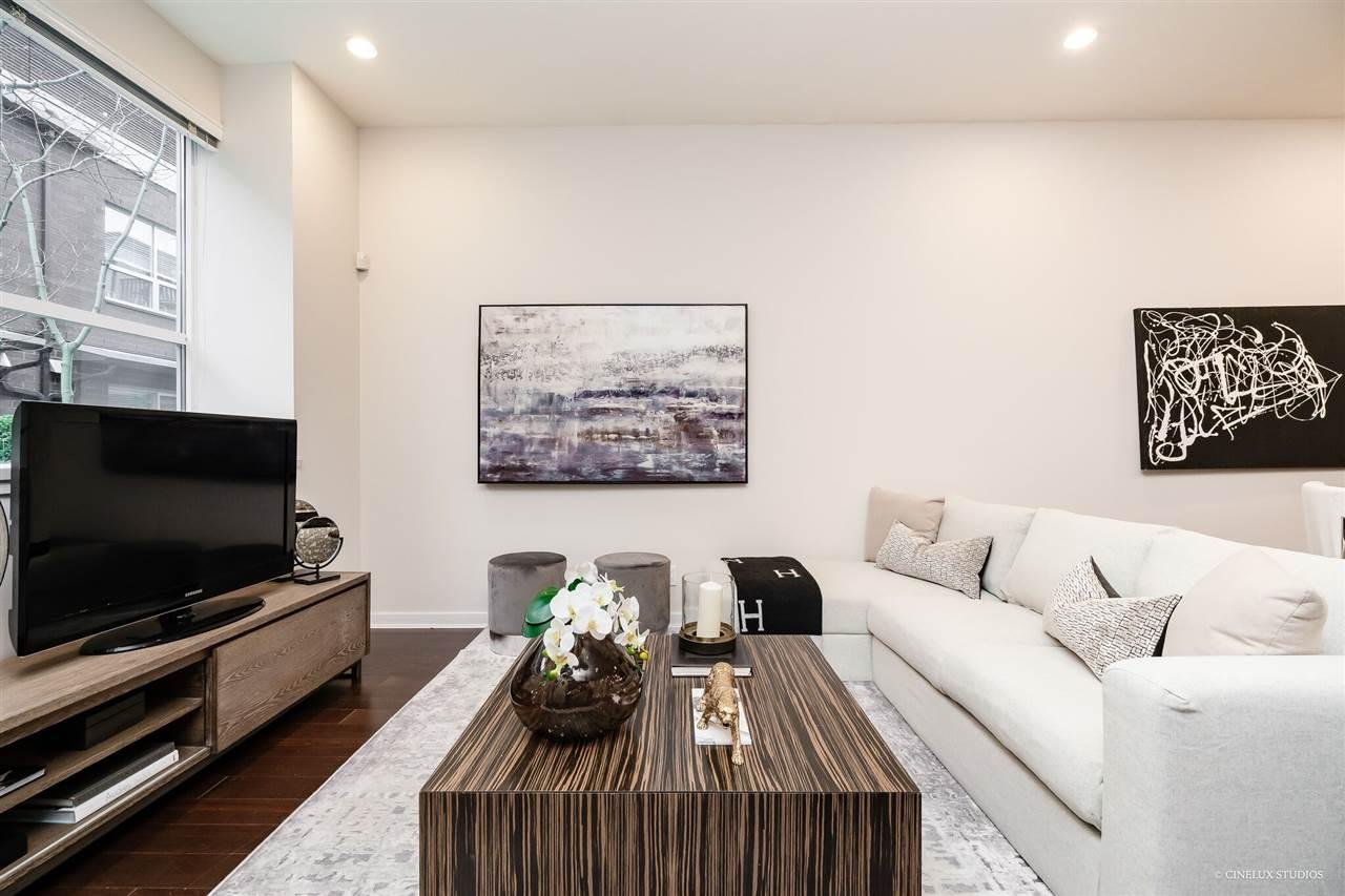 Modern living room with a white sofa, wooden coffee table, TV unit, and artwork on the walls, bright lighting.