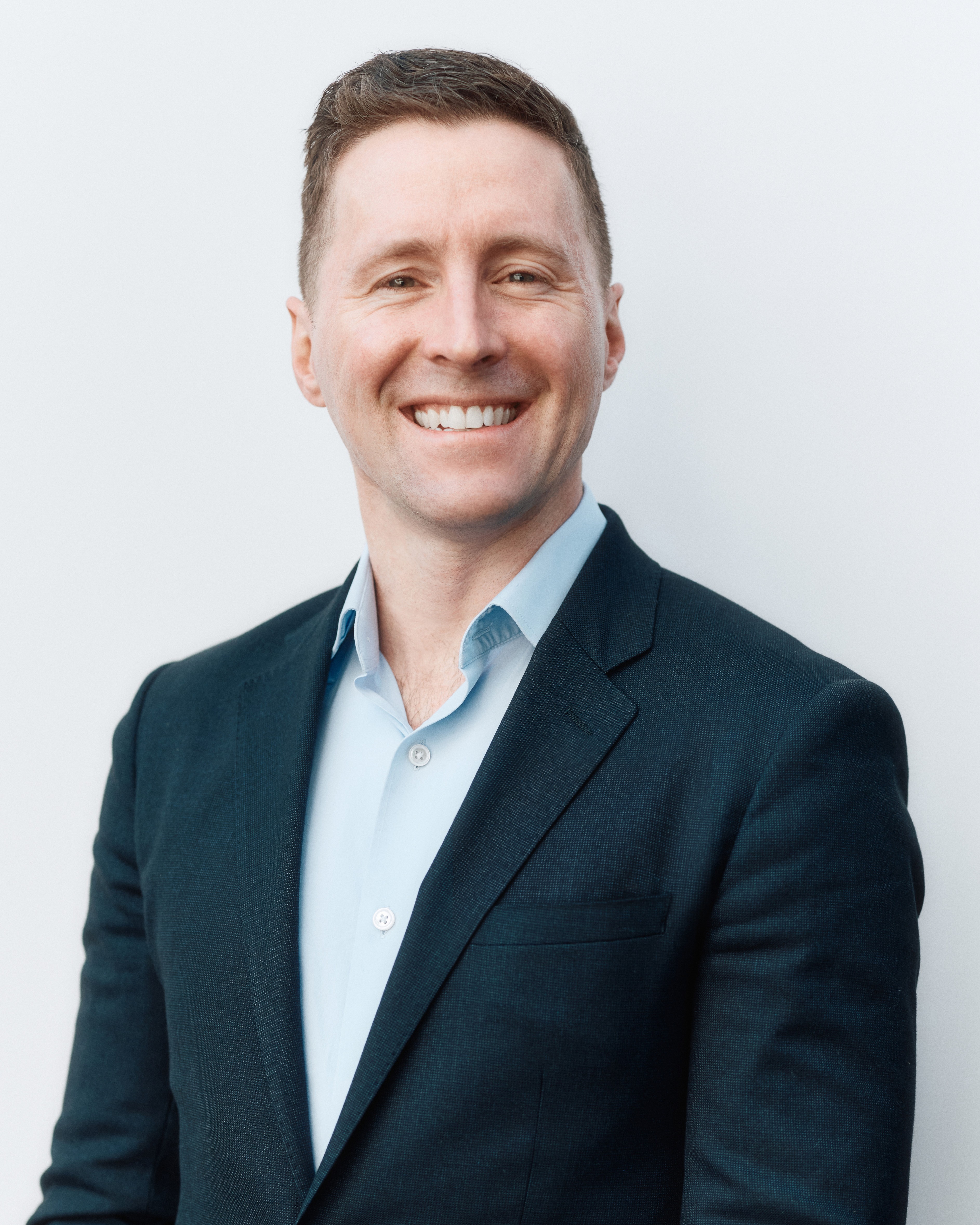 Woman in a blue blouse smiling gently in front of a softly lit backdrop, with abstract flowing light patterns creating a serene, professional atmosphere.