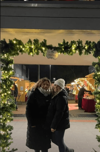 A person attentively paints a vibrant, expressive artwork of two people embracing, featuring bold colors like pink, blue, and green, highlighting themes of love and closeness in the painting.