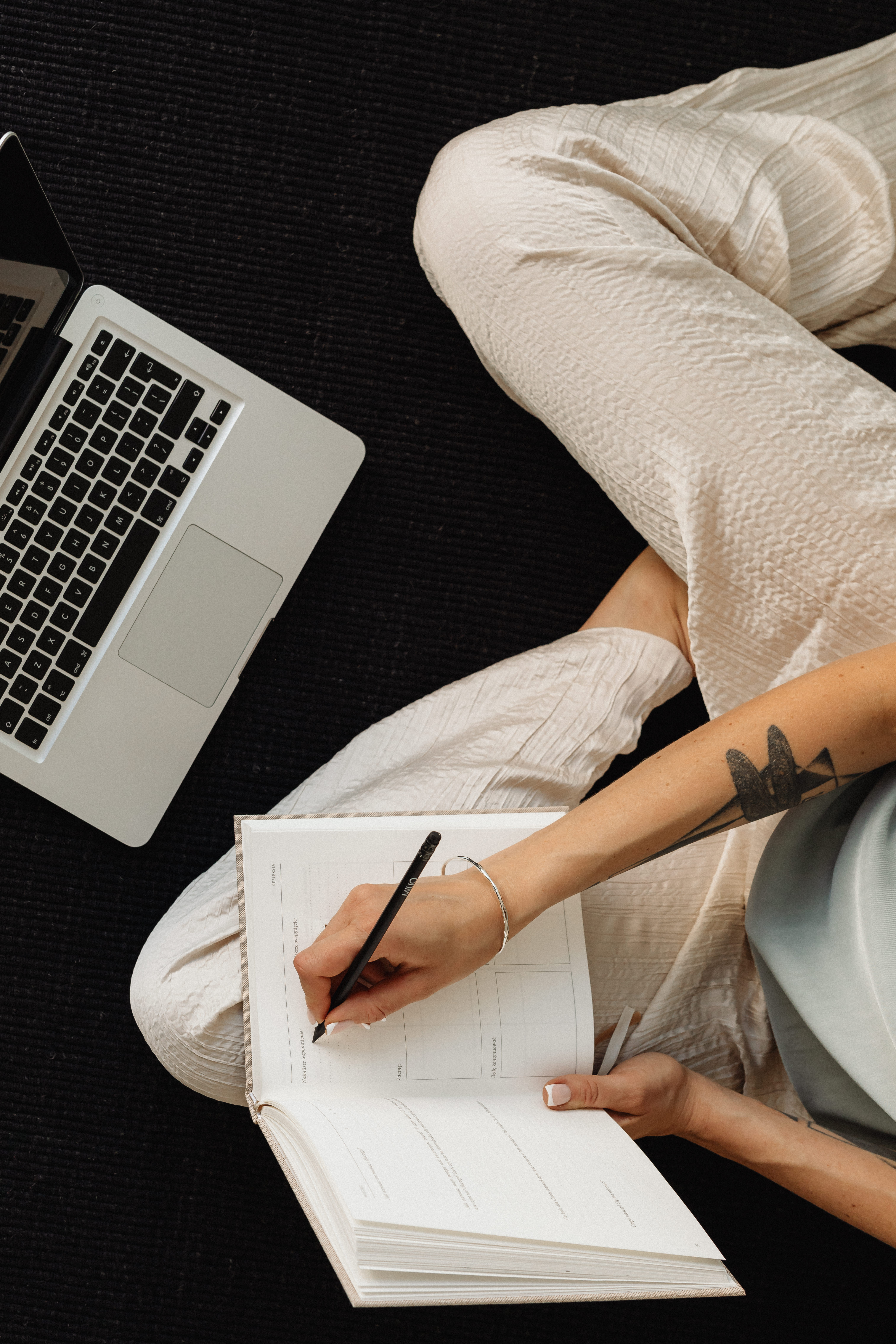 Top-down view of a person writing in a notebook beside an open laptop