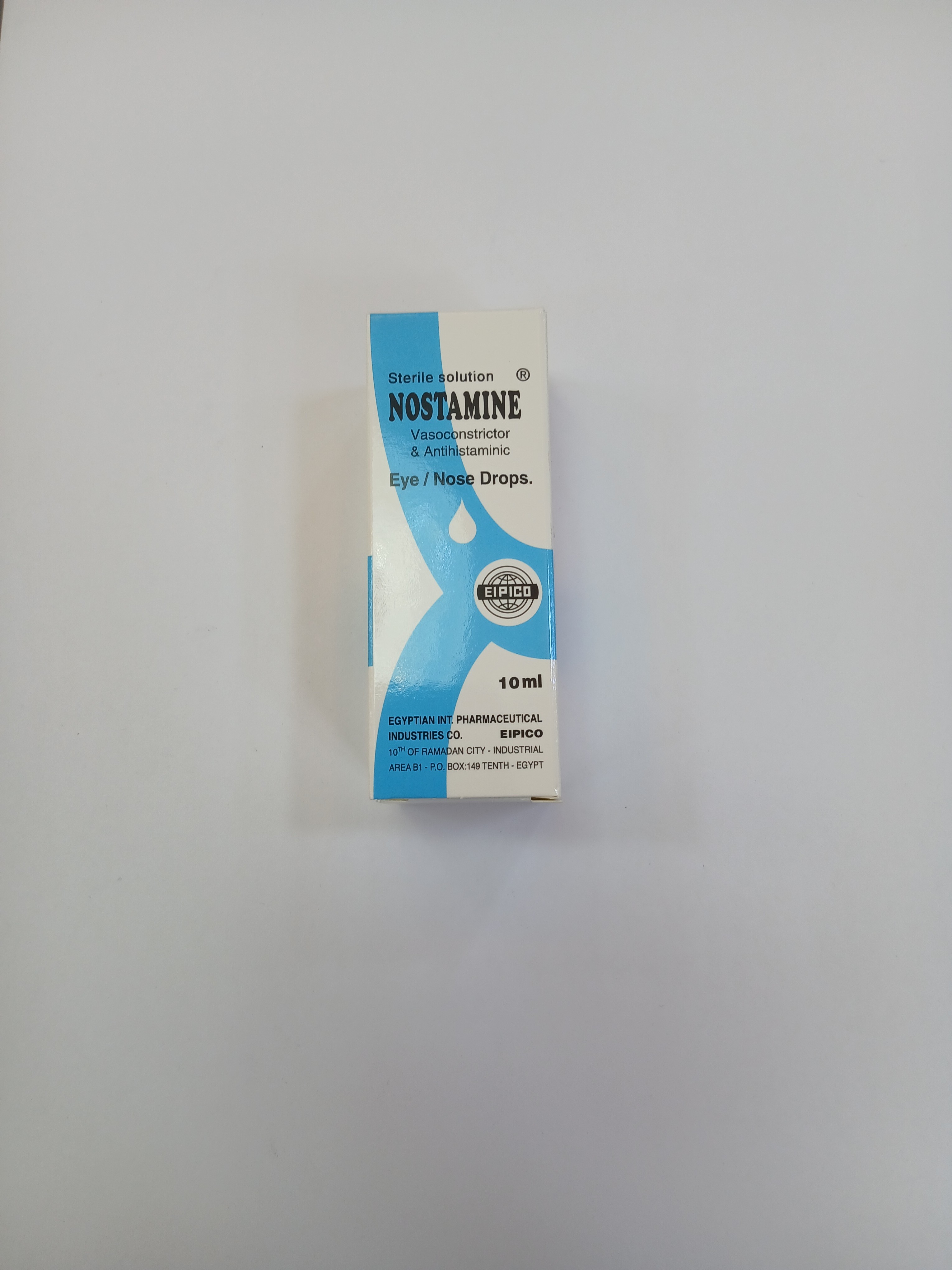 A small rectangular white and blue cardboard box packaging with a dropper bottle illustration and printed text in multiple languages stands upright against a plain light grey background.