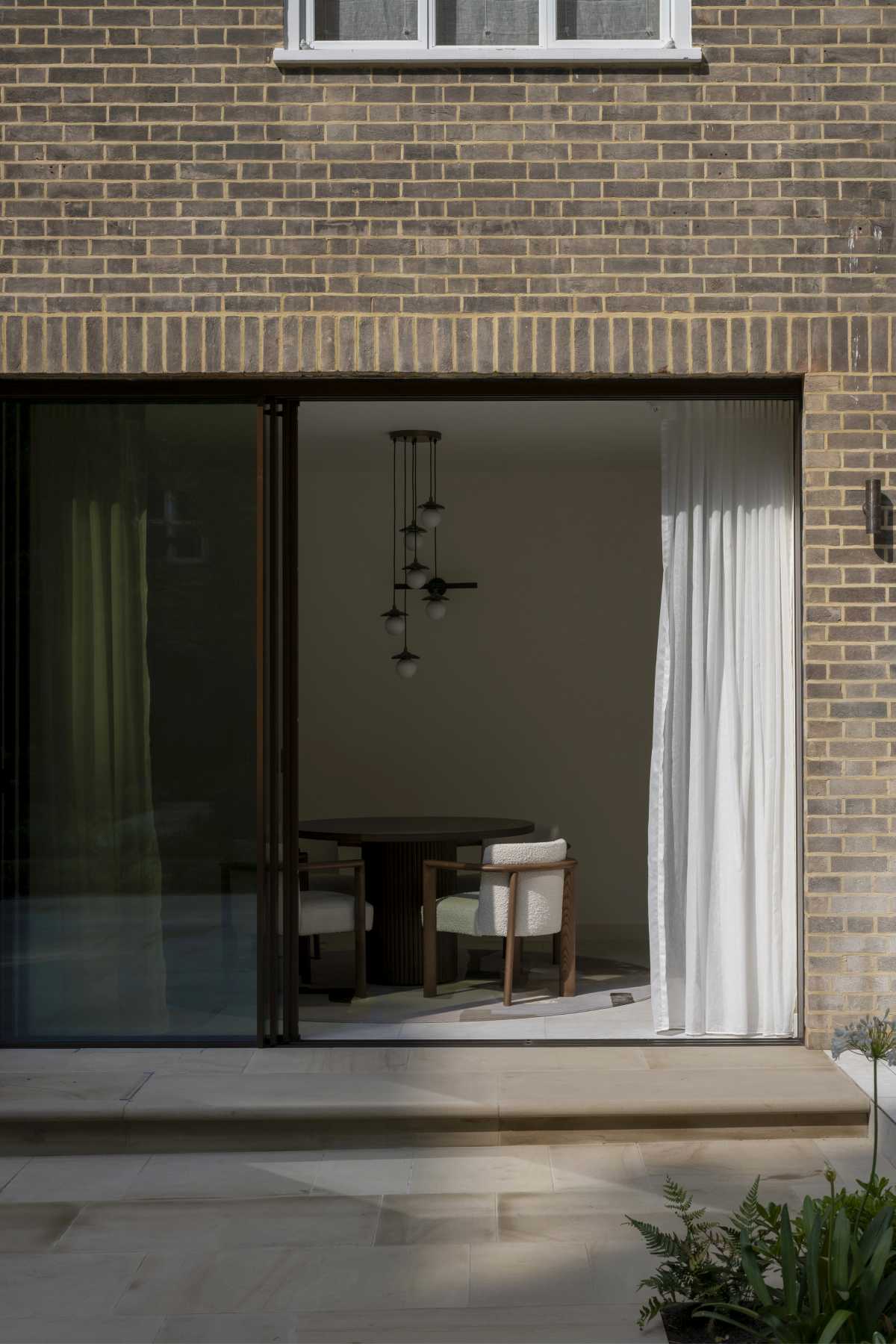 Contemporary glass patio doors seamlessly integrating a modern rear extension with a historic London brick property, designed by a bespoke conservation architect.