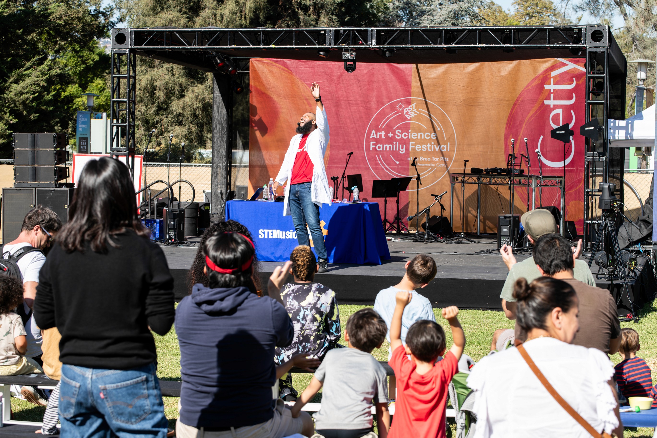 Families enjoying an outdoor stage performance at the Art + Science Festival, a community event produced by Tiffany Onyeyiriuche.