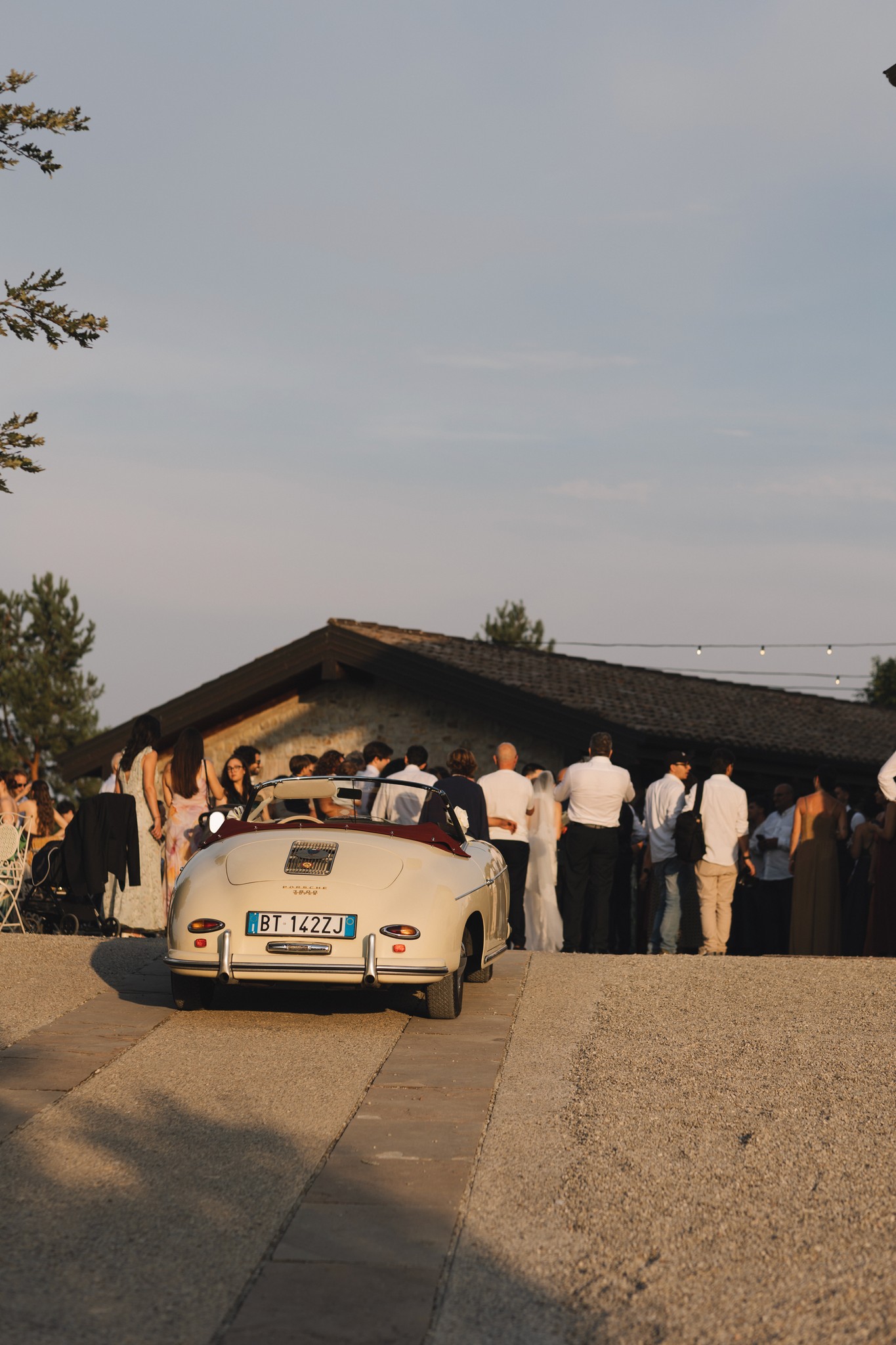 Sposi in auto d'epoca a Parco di Montebello, invitati in festa sullo sfondo durante il reportage matrimoniale