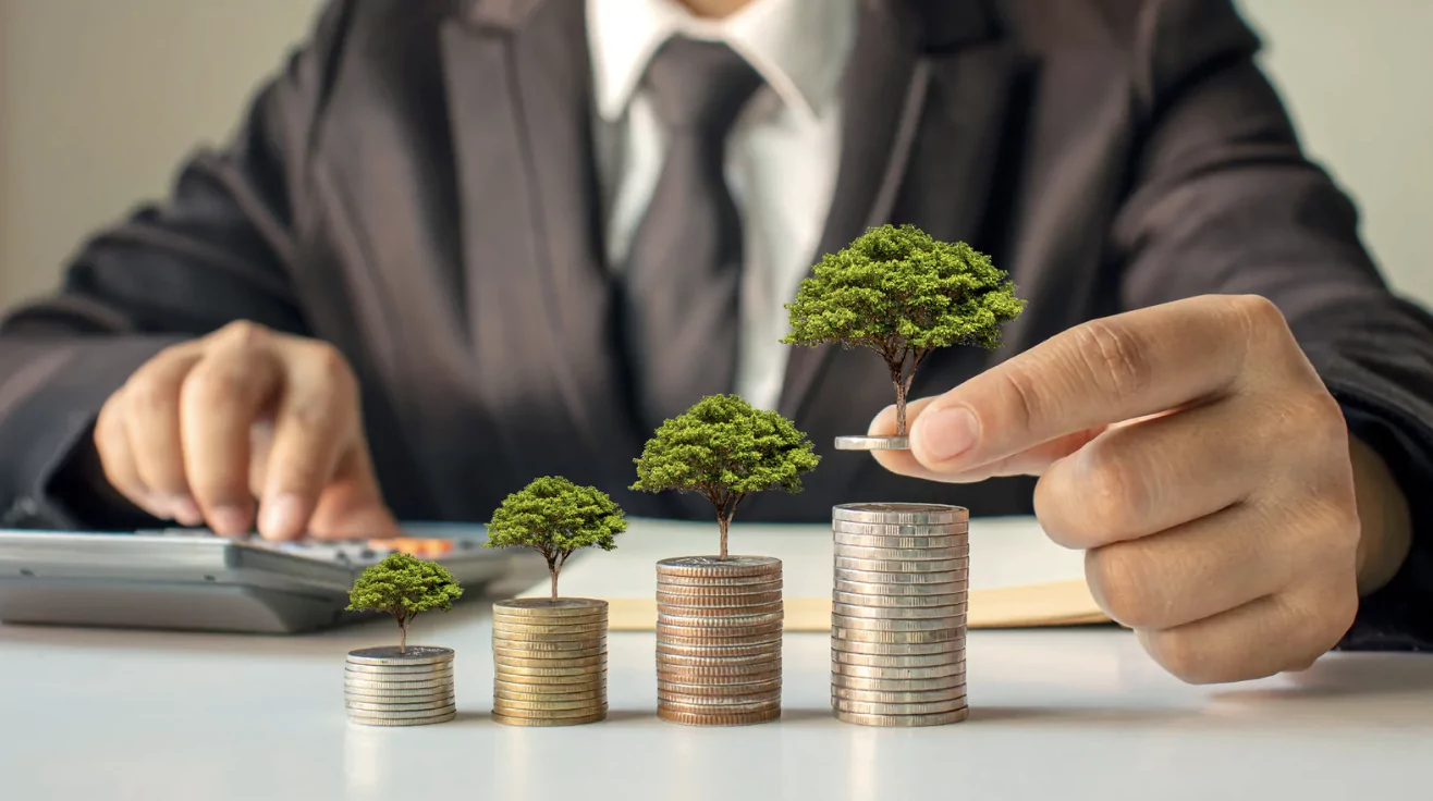 guy holding tiny trees on top of coin stacks