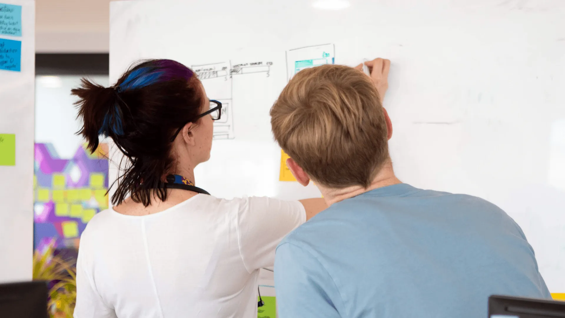 A woman writes on a white board as another person looks on