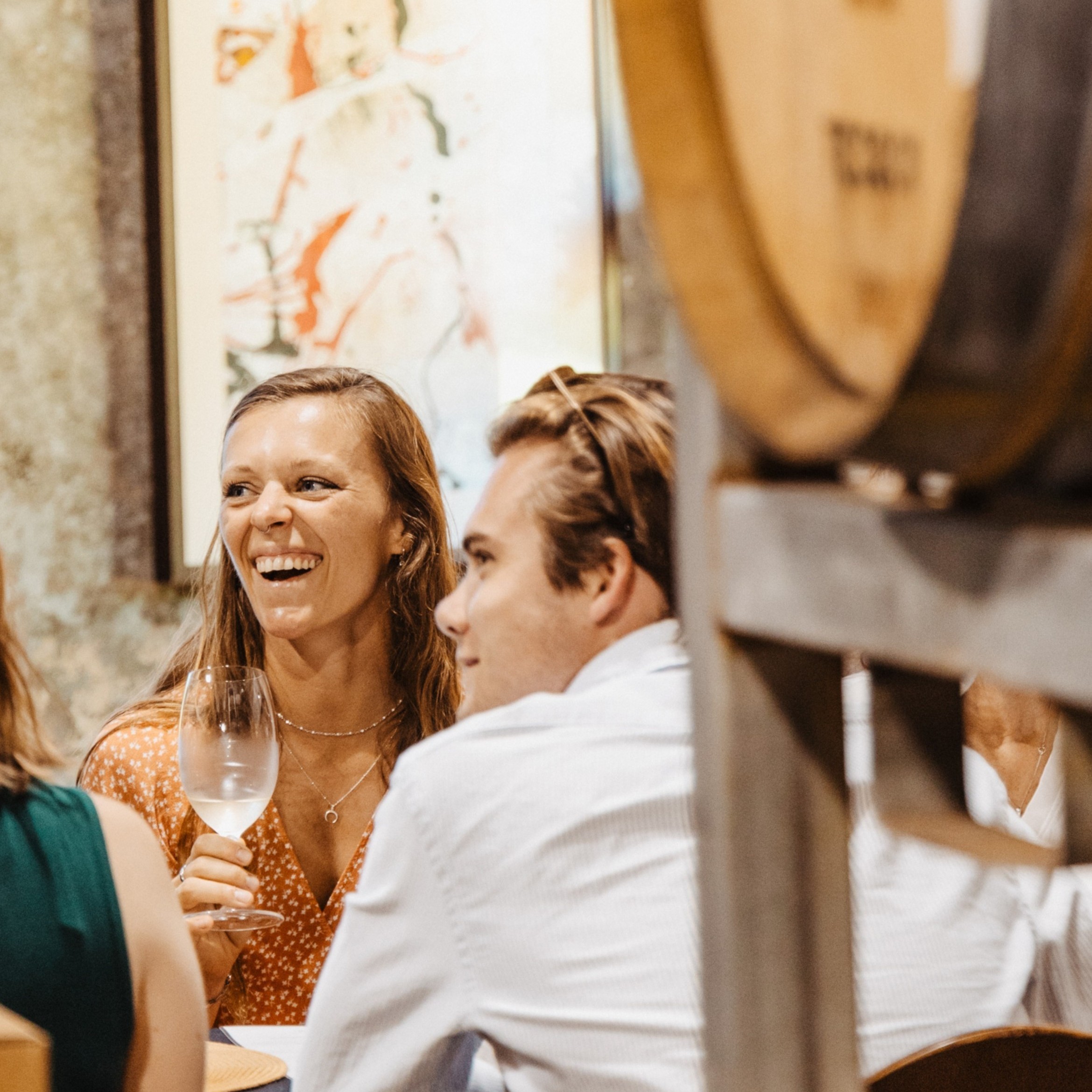 Lady in summer dress laughs during a wine tasting in a barrel room with artwork in the background