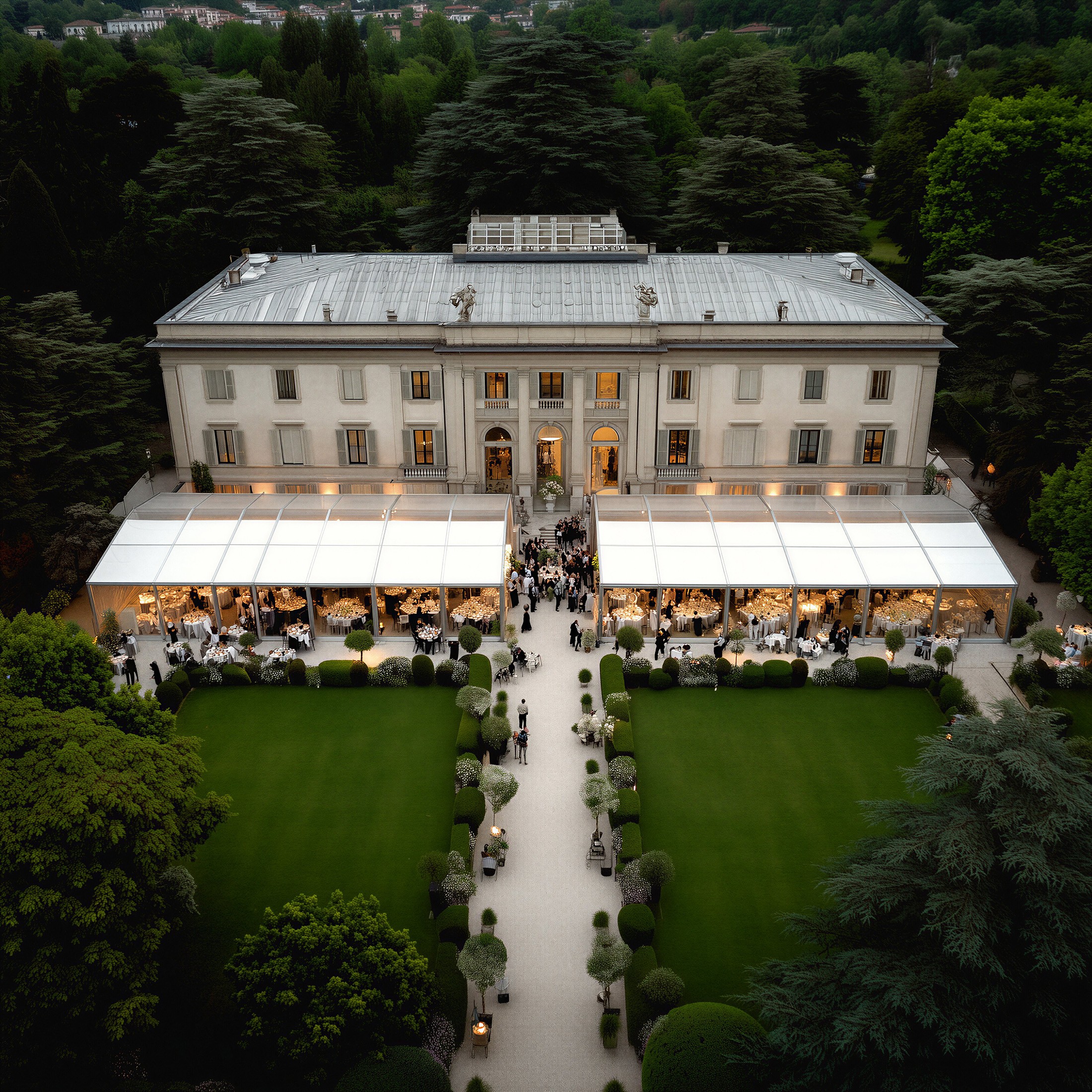 A grand mansion surrounded by greenery, featuring a well-maintained garden and outdoor seating areas.
