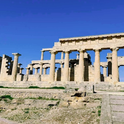 晴朗湛蓝的天空下，古老的石砌神庙遗址立有柱廊，四周环绕着草地和起伏不平的石质地面。