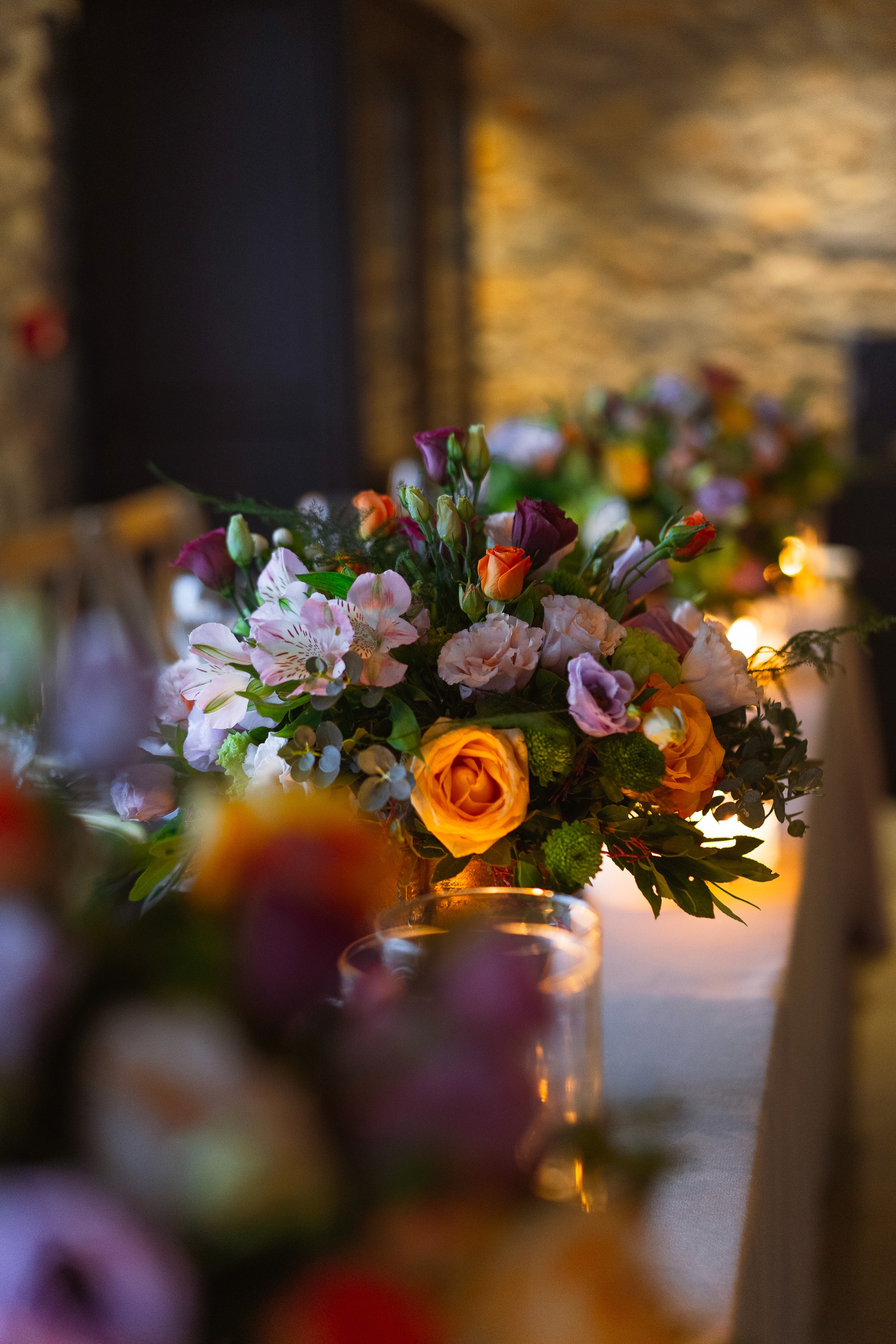 Close-up of a bespoke colorful floral centerpiece with orange roses on a luxury wedding reception table in a Greek stone venue