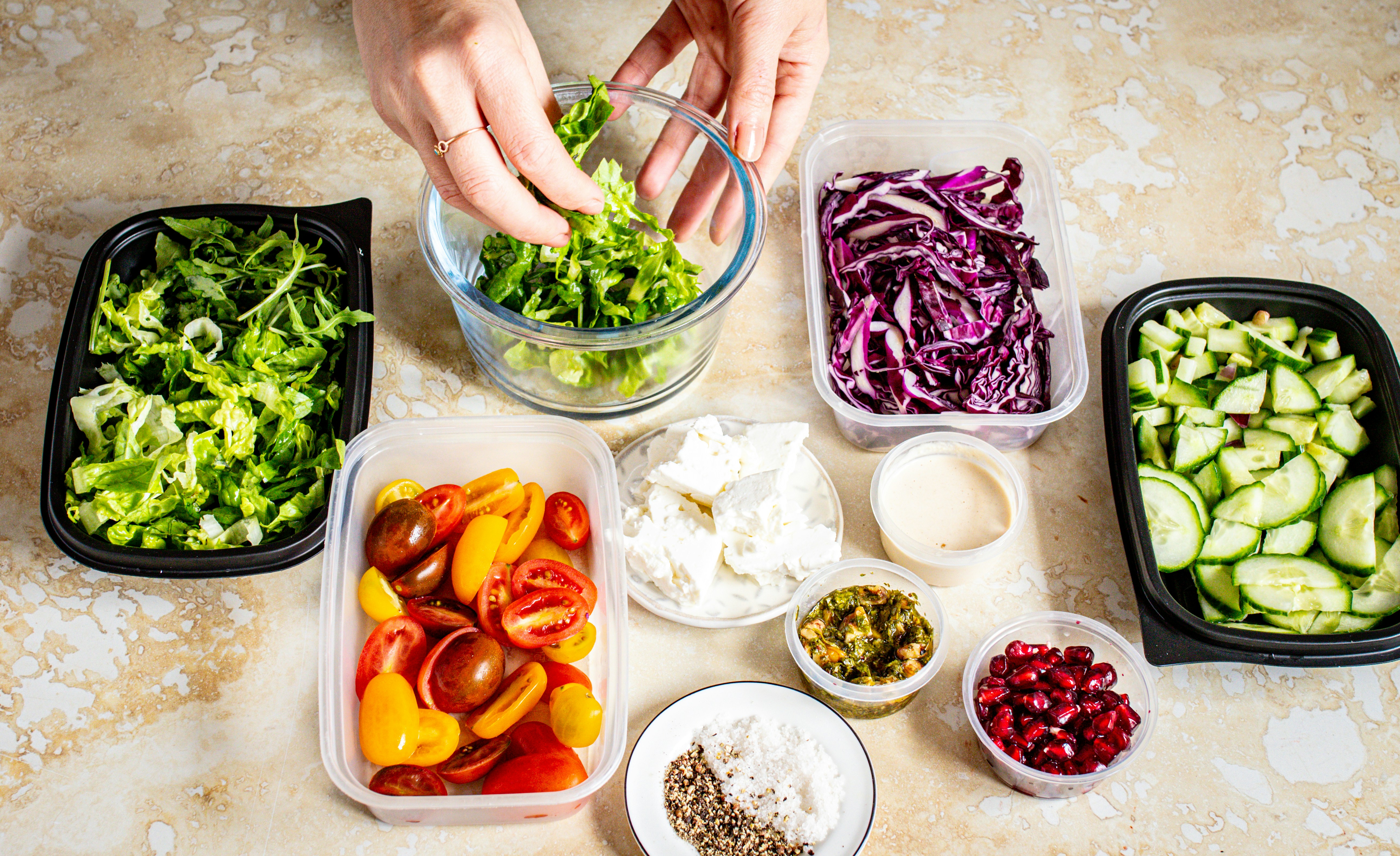 Hands preparing a salad with meal prep ingredients in containers.