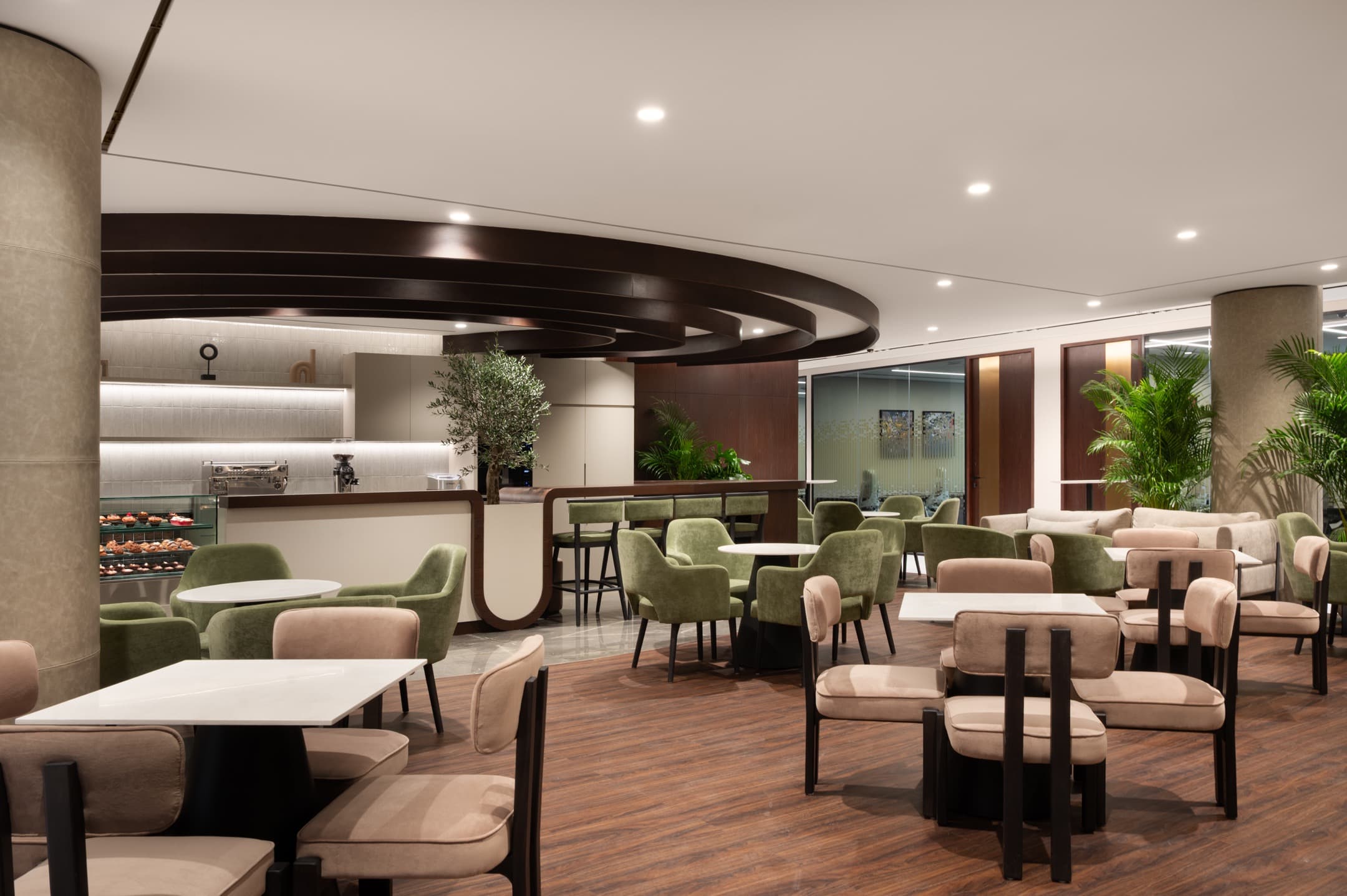 Modern office lounge of Office Square in Dubai with green and beige seating, coffee tables, a wooden bar counter, and integrated café space featuring natural decor and warm lighting.