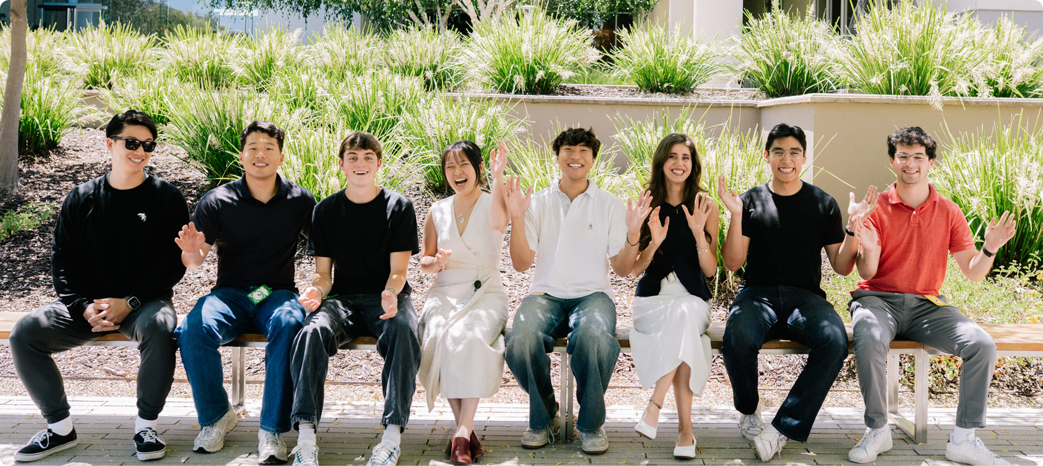 Two silhouetted figures stand facing a sunset, with a package-carrying Wing delivery drone above them.