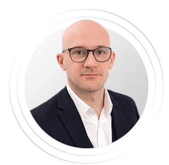 A professional man with glasses and a light suit is shown against a neutral background.