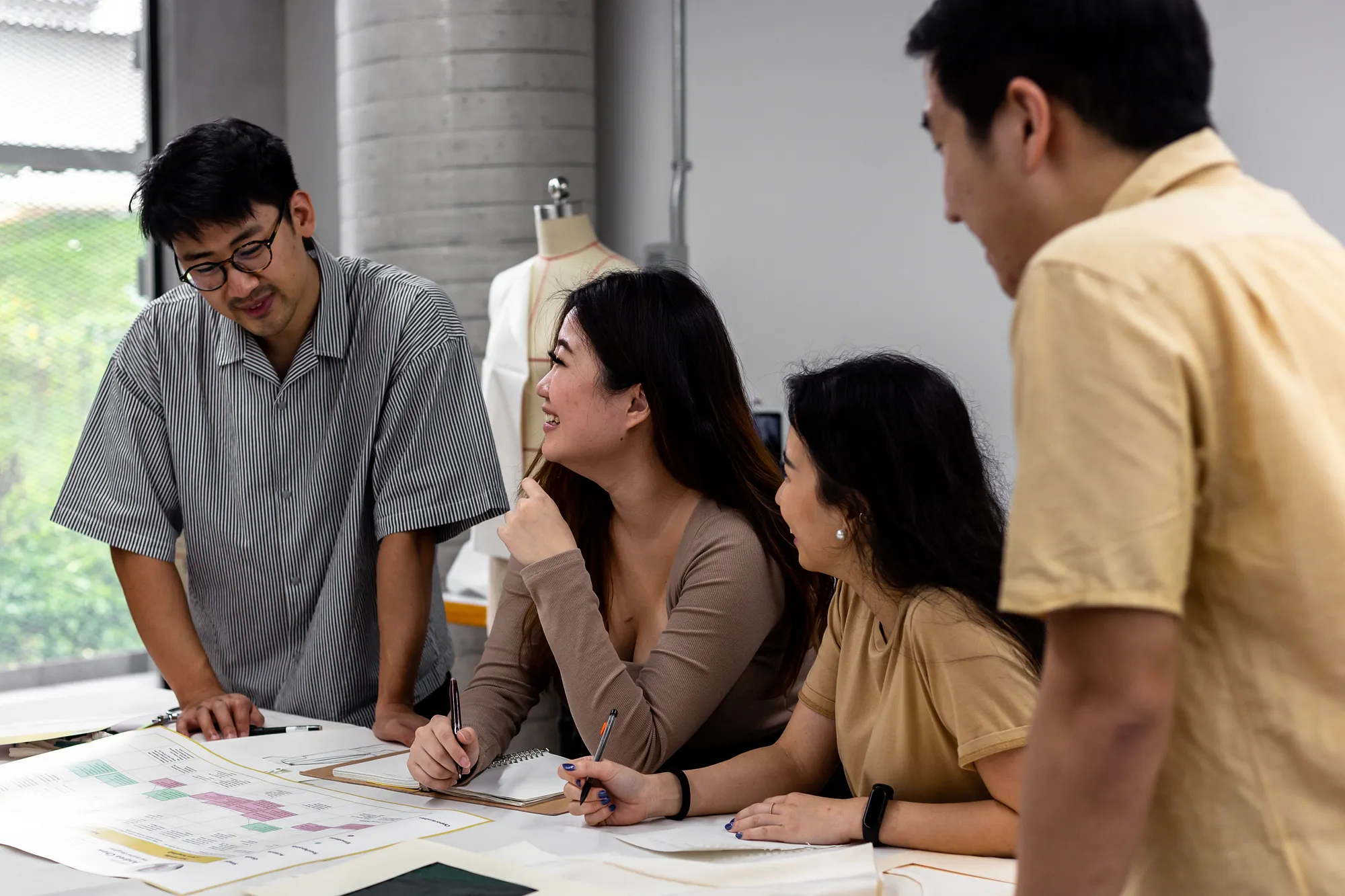 A group of people surrounding a table, having a discussion.