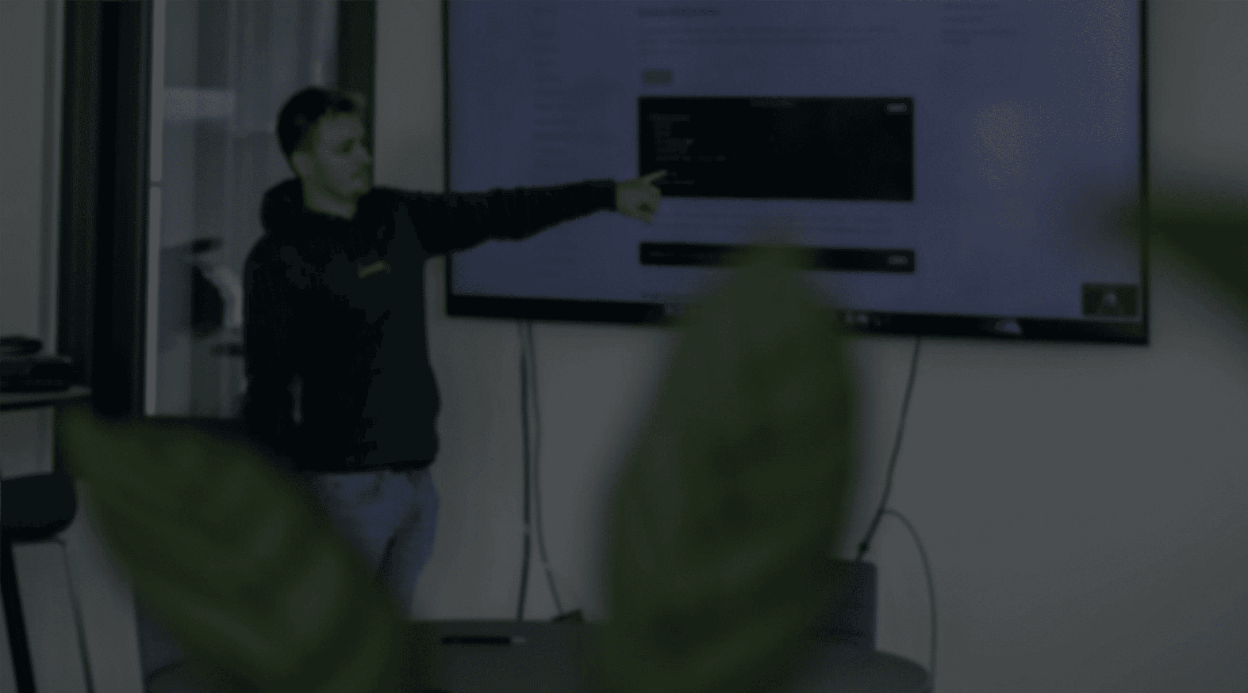 Eine Person steht vor einem Fernseh und zeigt auf einen Codesnippet und erklärt dabei etwas