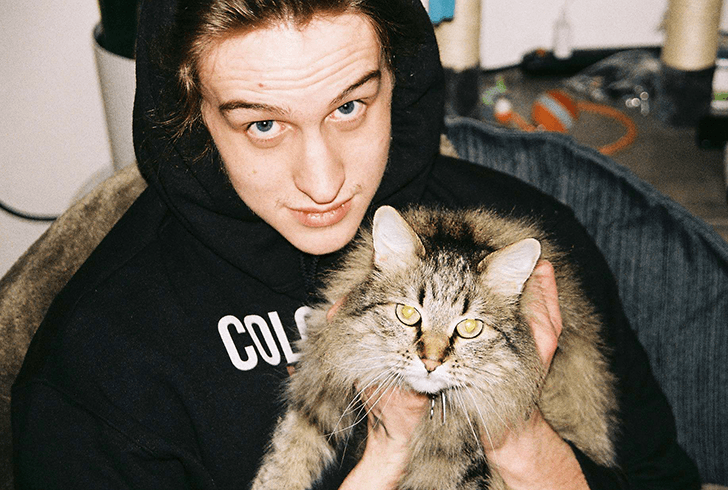 Cooper sits looking up at the camera, holding his friend's brown cat Hazel.