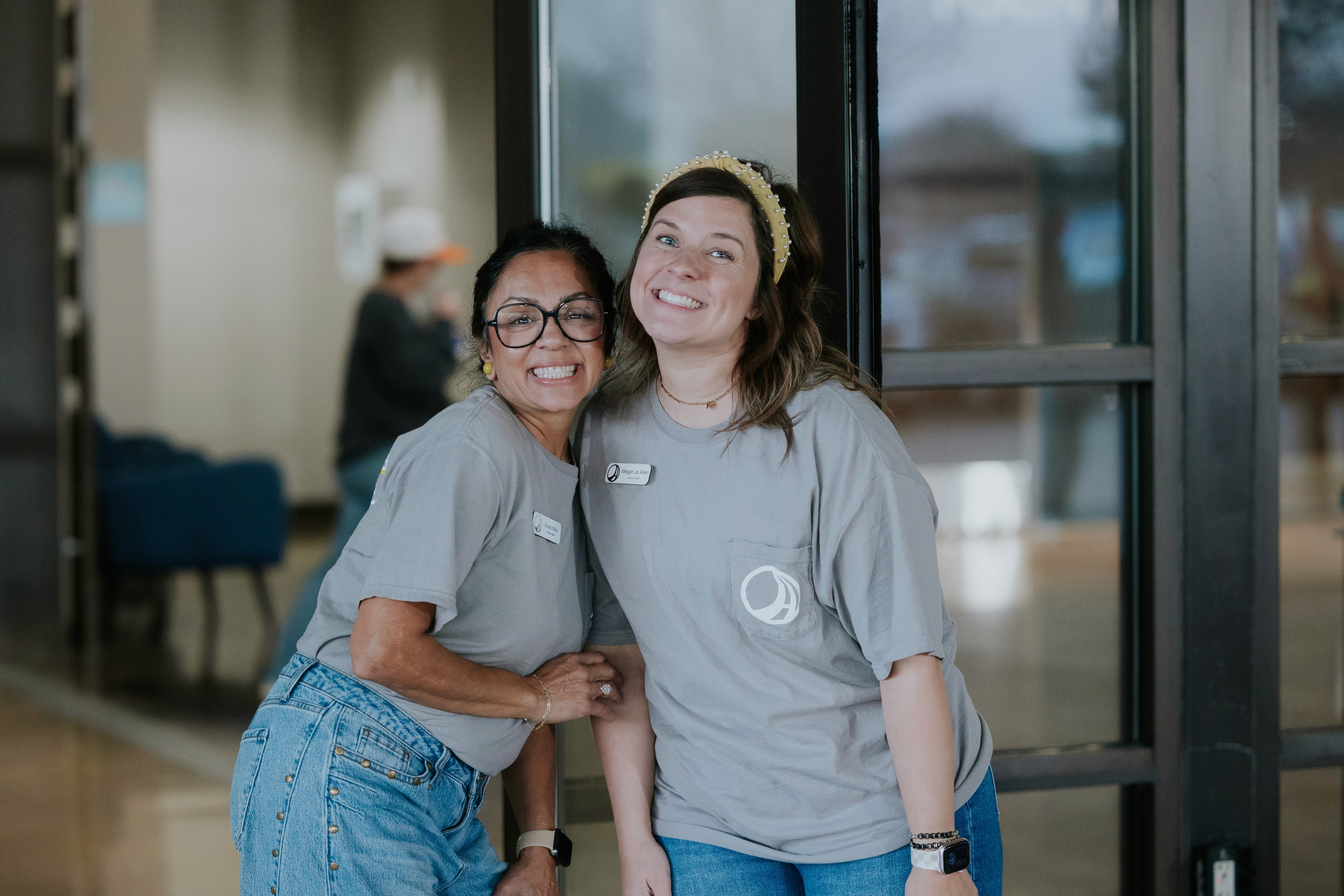 Three individuals stand together outdoors, smiling, with a modern building in the background.