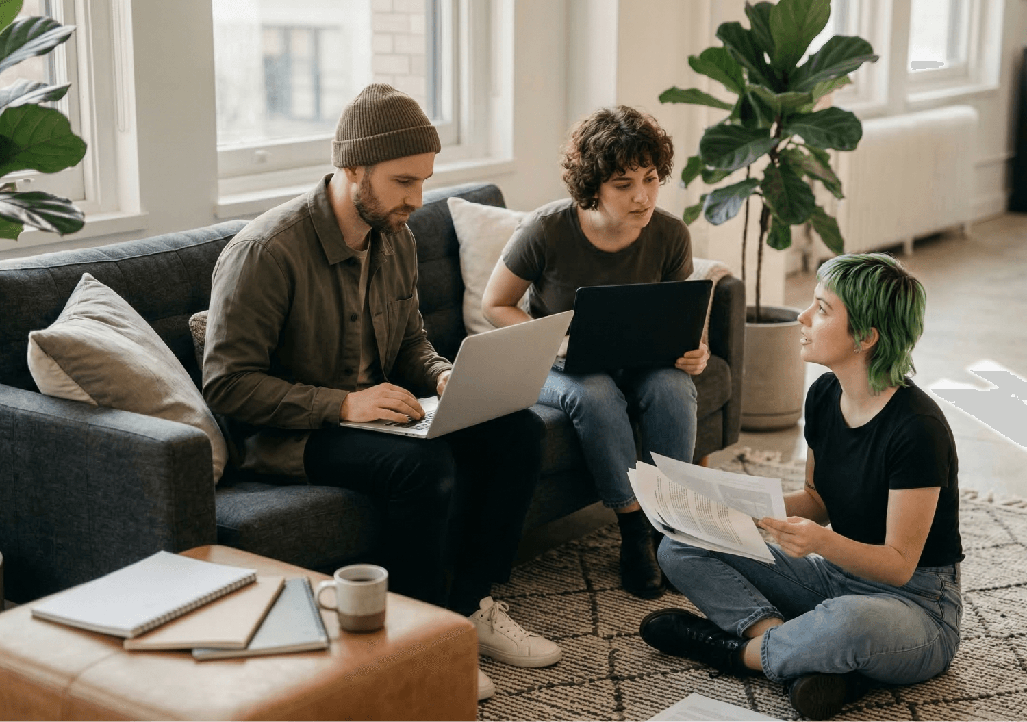 Three colleagues collaborating with laptops and documents in a casual office lounge