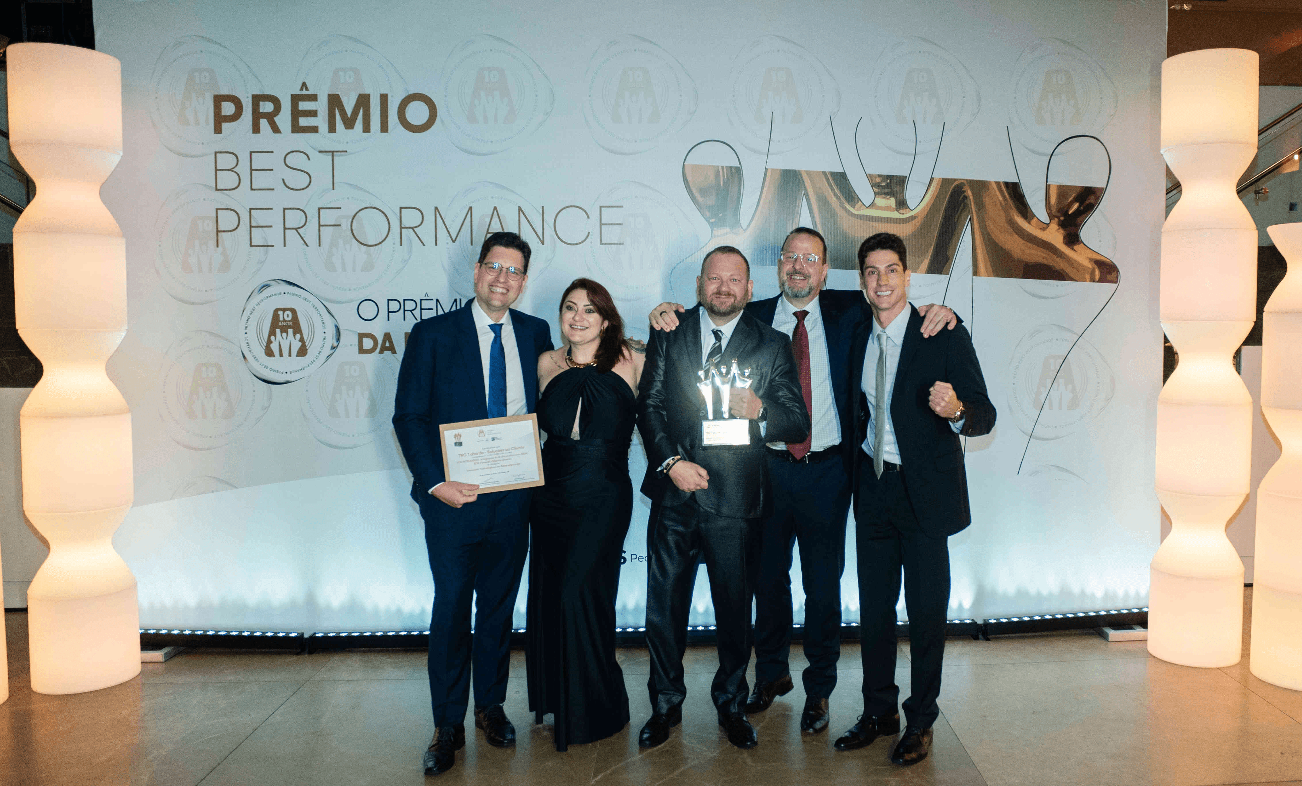 Executivos da TRC Taborda posando com troféu ouro e certificado no palco do Prêmio Best Performance 2025