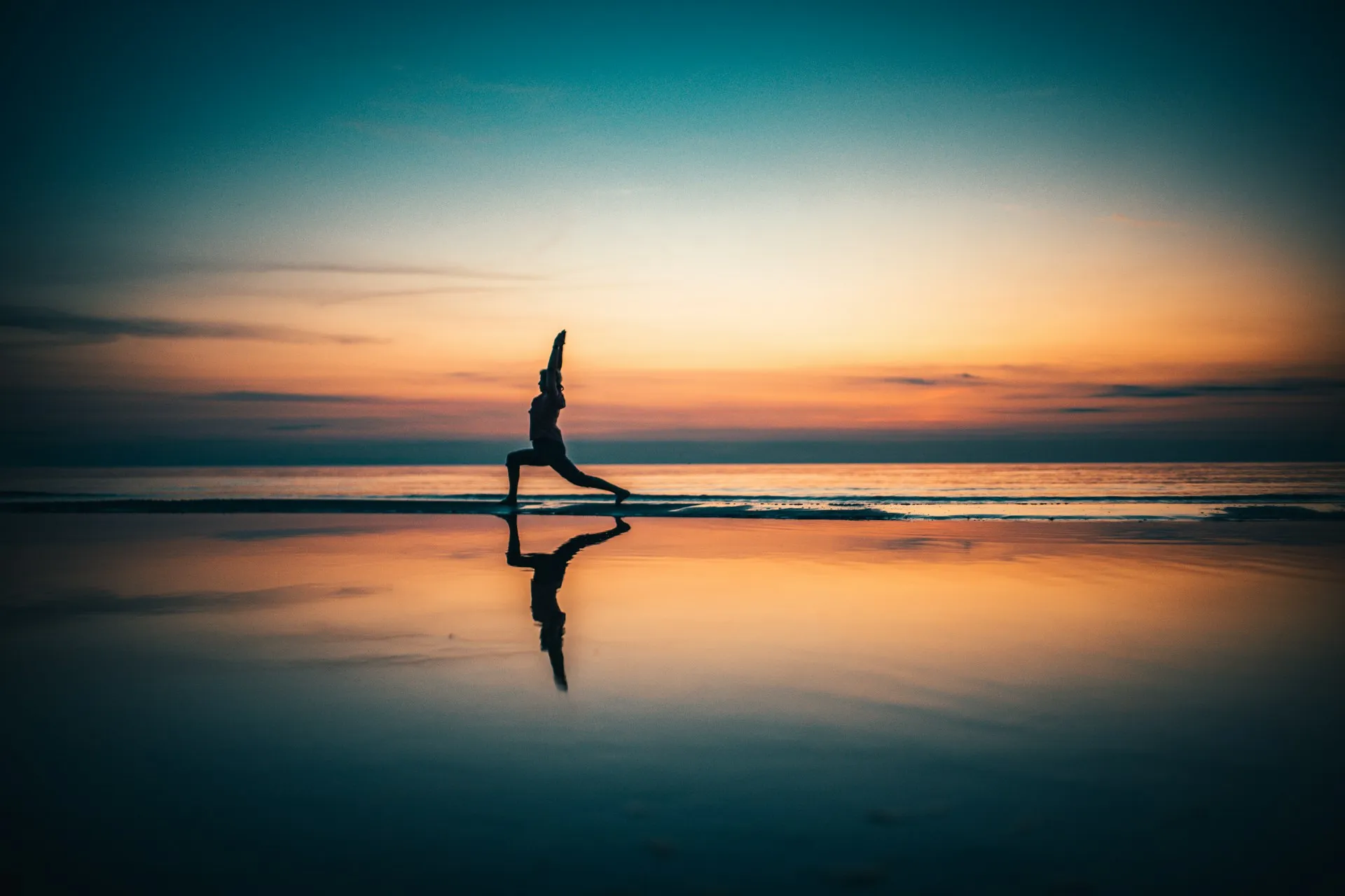 Person practicing yoga on the beach at sunset with calm ocean reflection