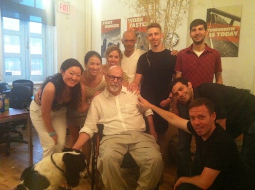 A photo of a group of students and a dog sitting around an old teacher.