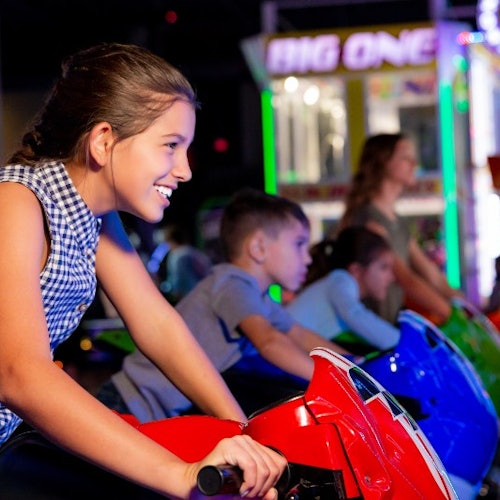 Деца, които се усмихват и играят на аркадни игри с мотоциклетни състезания в слабо осветен увеселителен център.