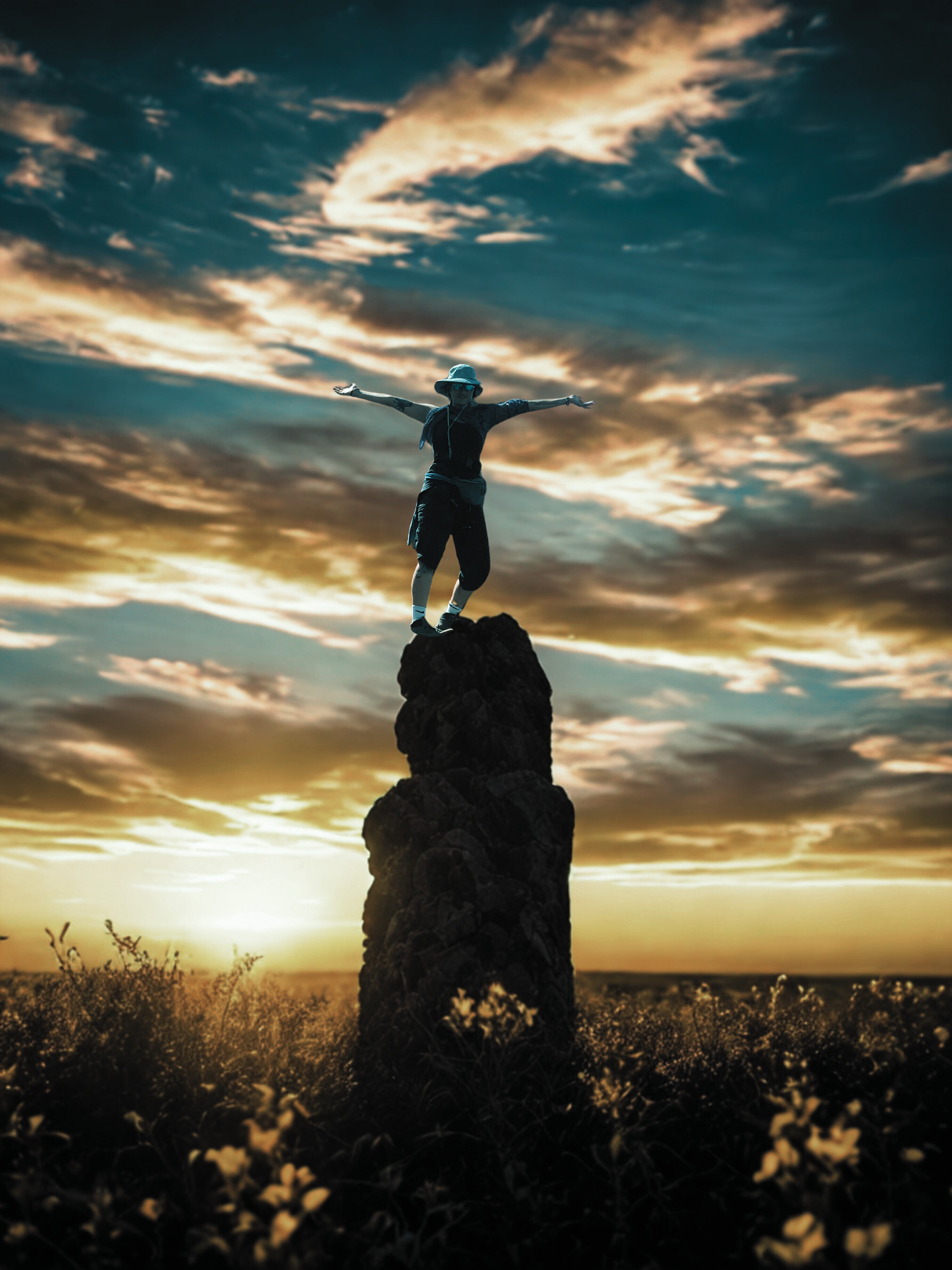 A young person with curly hair smiles at the camera while sitting in front of a laptop against a dark background.