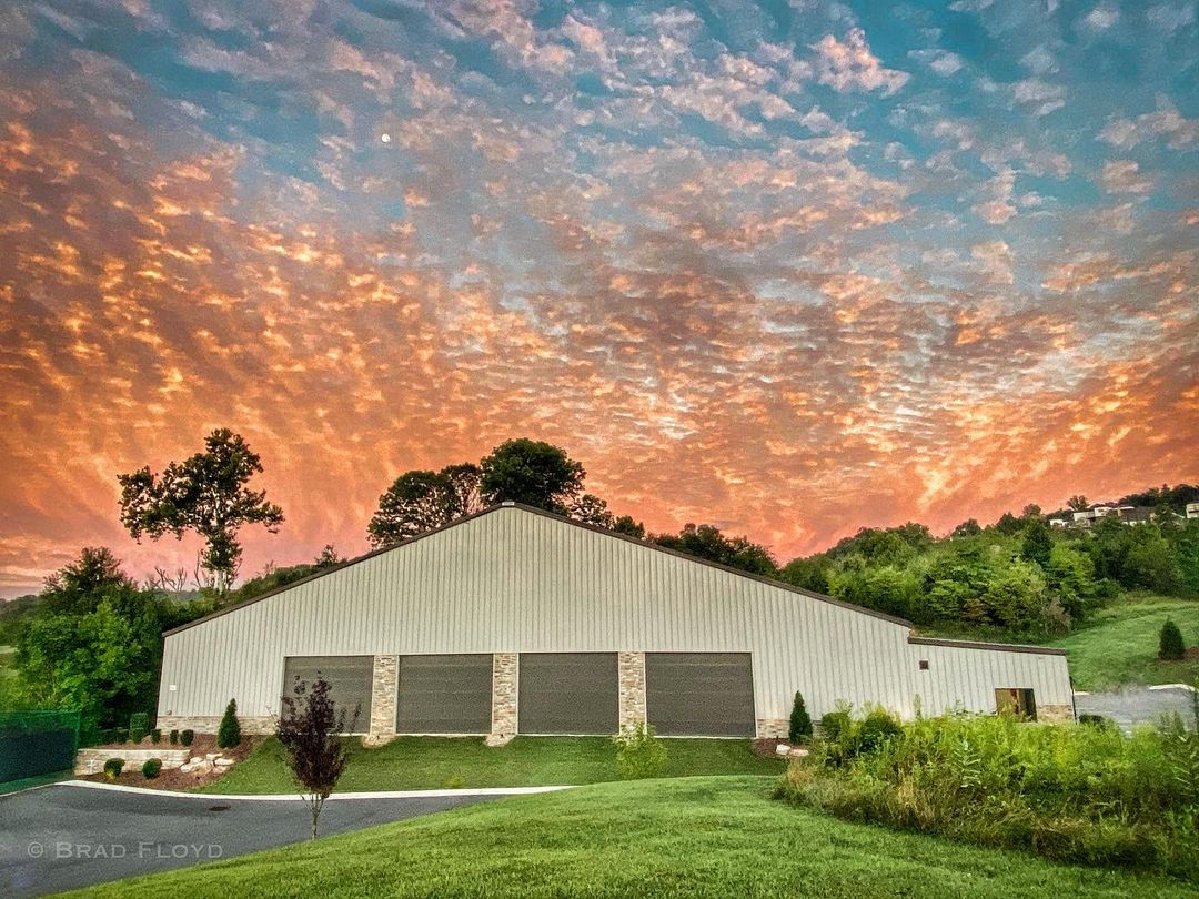 A large building with garages under a colorful sunset sky, surrounded by green grass and trees.