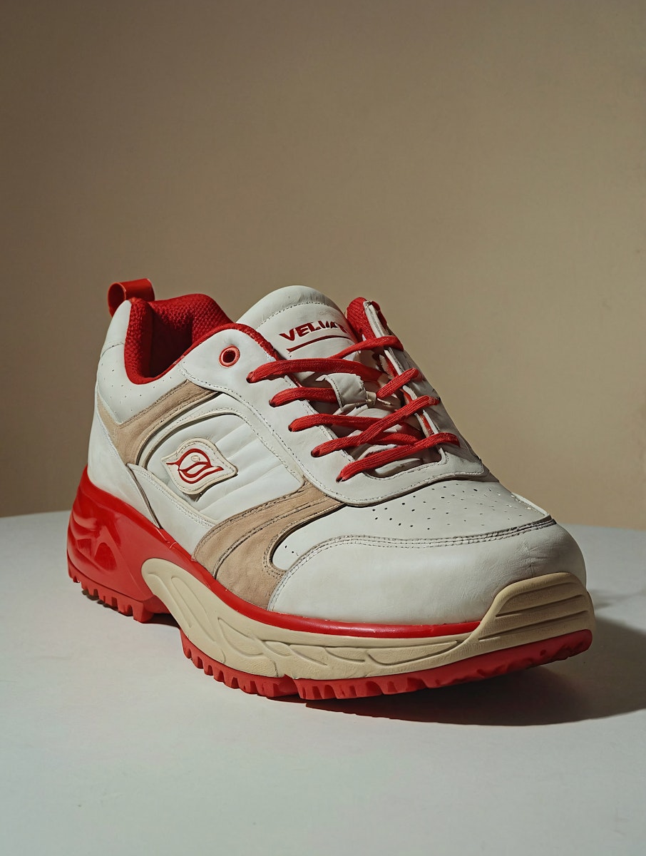 A white and red chunky sneaker with red laces and a bold red rubber sole, displayed on a clean white surface against a beige background.