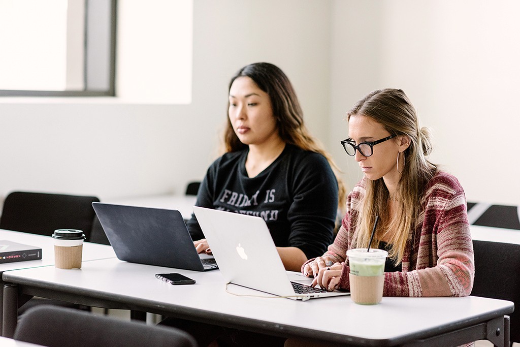 Two collaborators working side by side at laptops, focused and in sync on a shared task.