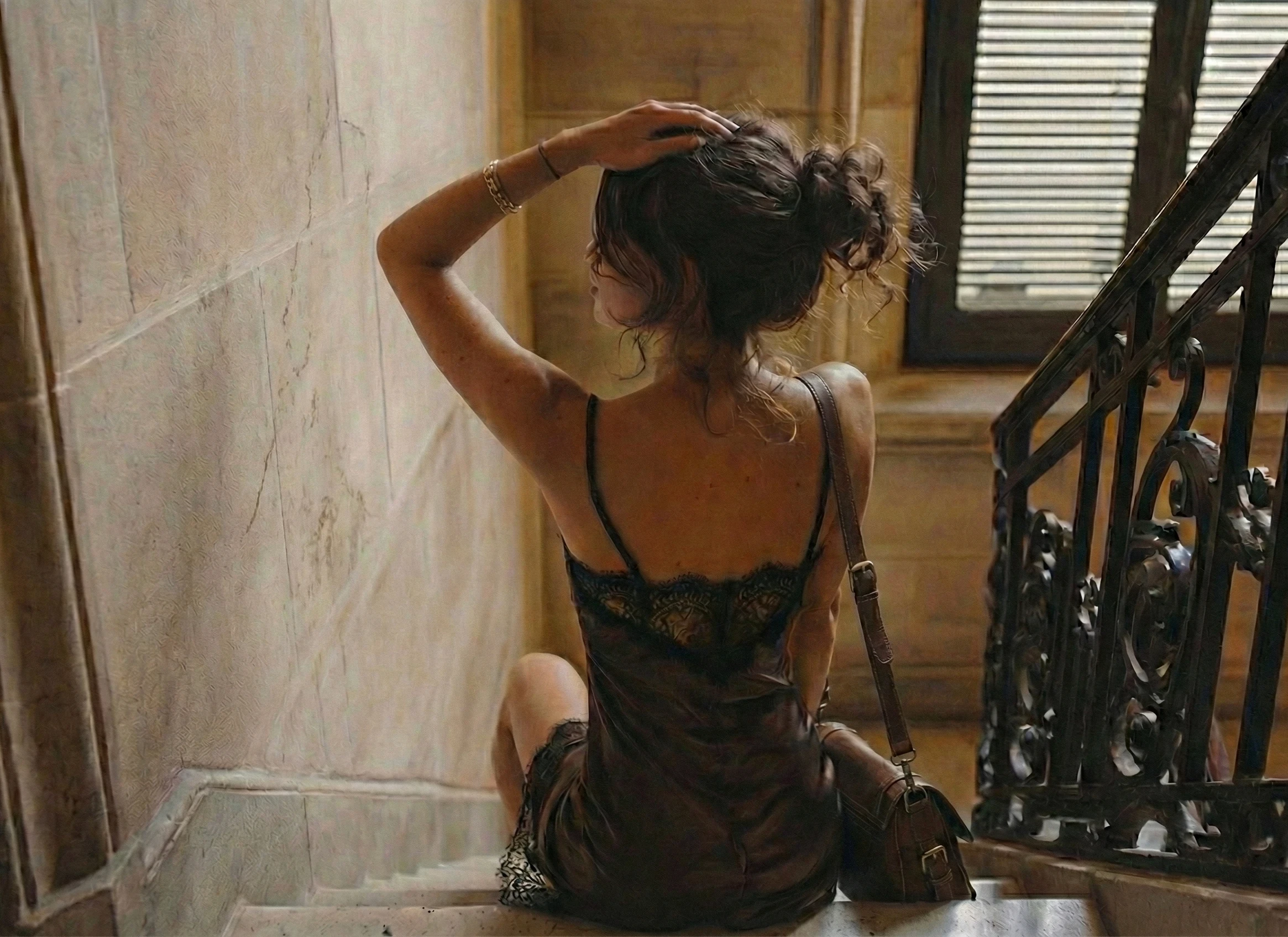 Woman in a lace slip dress seated on a staircase, seen from behind.