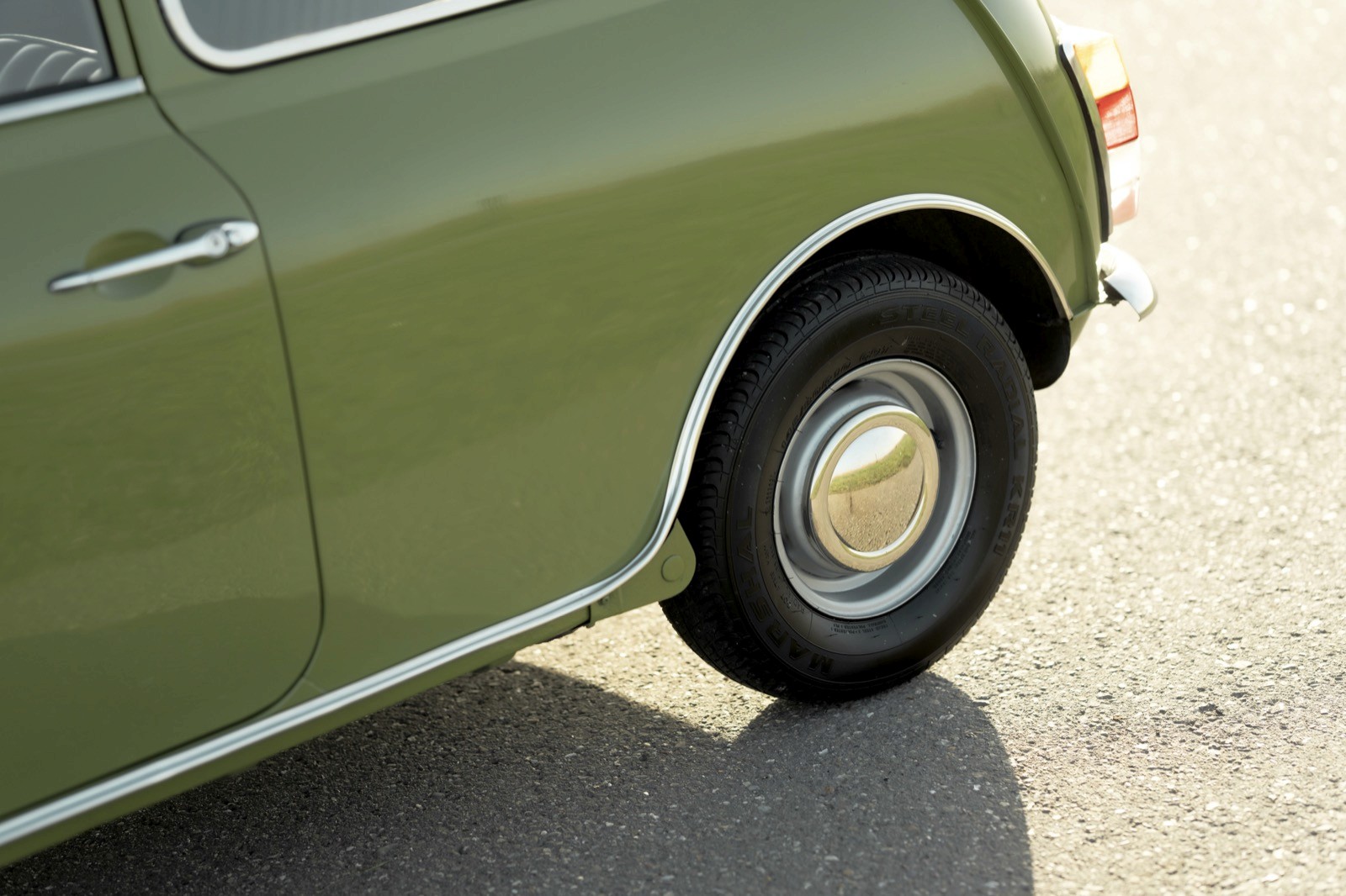 A close-up view of the wheel and lower part of a green vintage car parked on a light-colored surface.