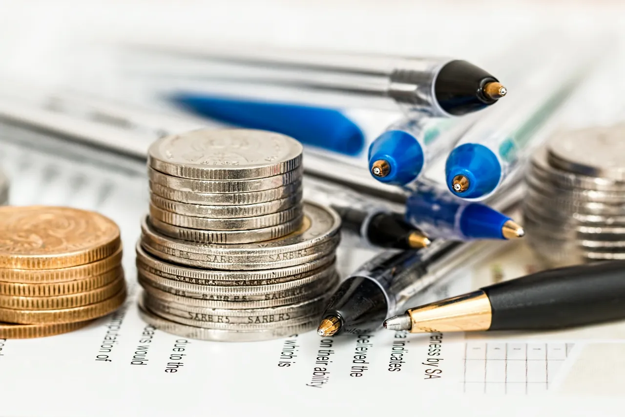 A close-up shot of stacks of coins and multiple ballpoint pens resting on financial document sheets.