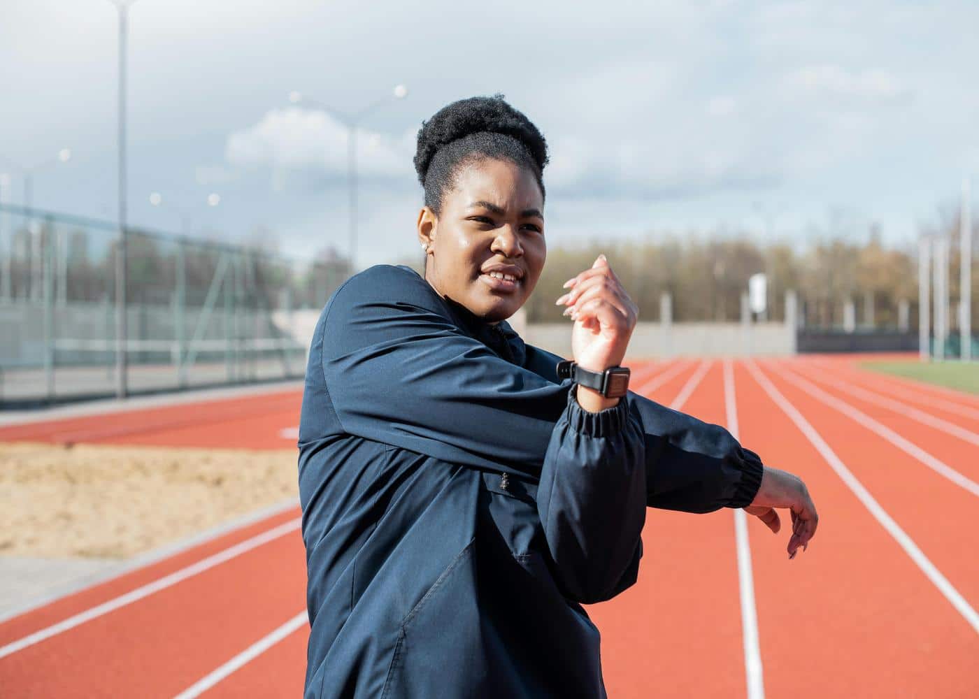 A woman wearing a smart watch on a running track stretching her arms