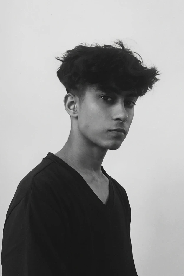 A thoughtful young person with dark hair gazes to the side, captured in soft black and white lighting.