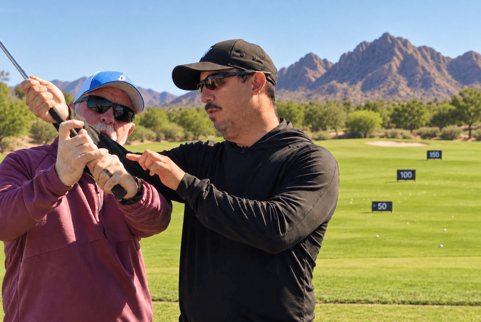 Coach adjusting a golfer's club position on the range, mountains in the background