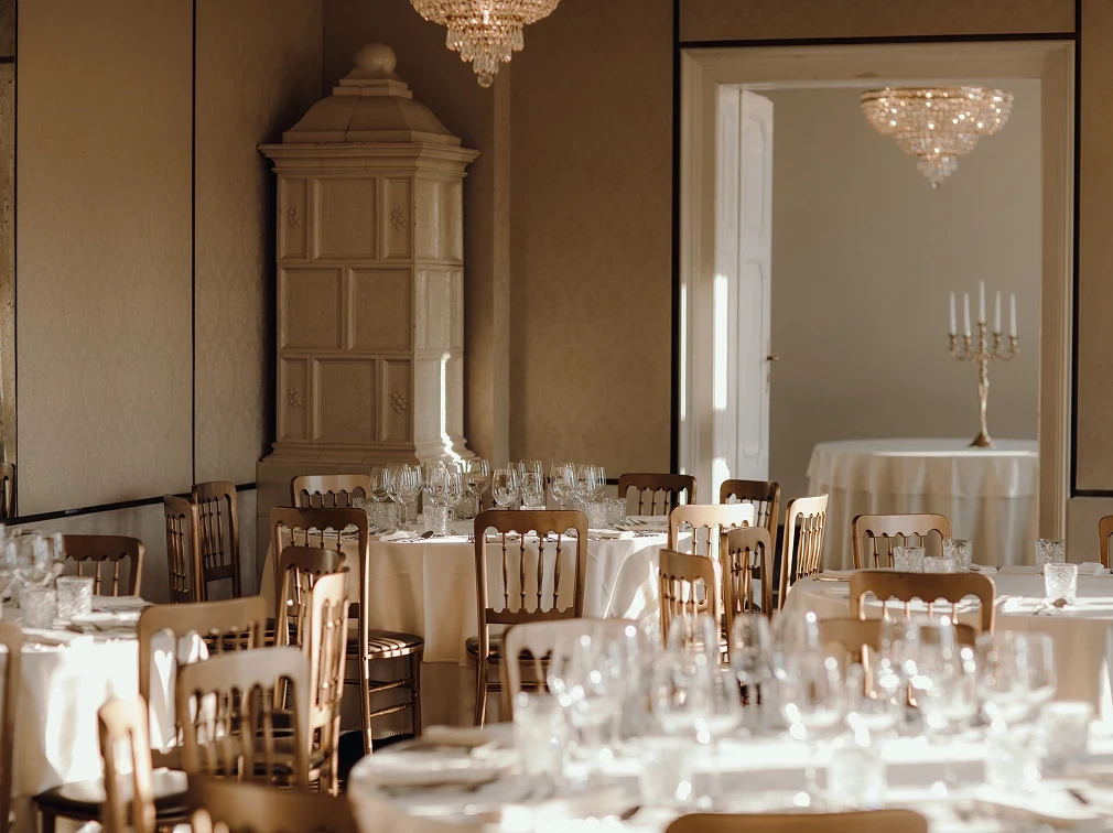 alt="Банкетный зал с белыми скатертями, деревянными стульями и винтажной печью на фоне