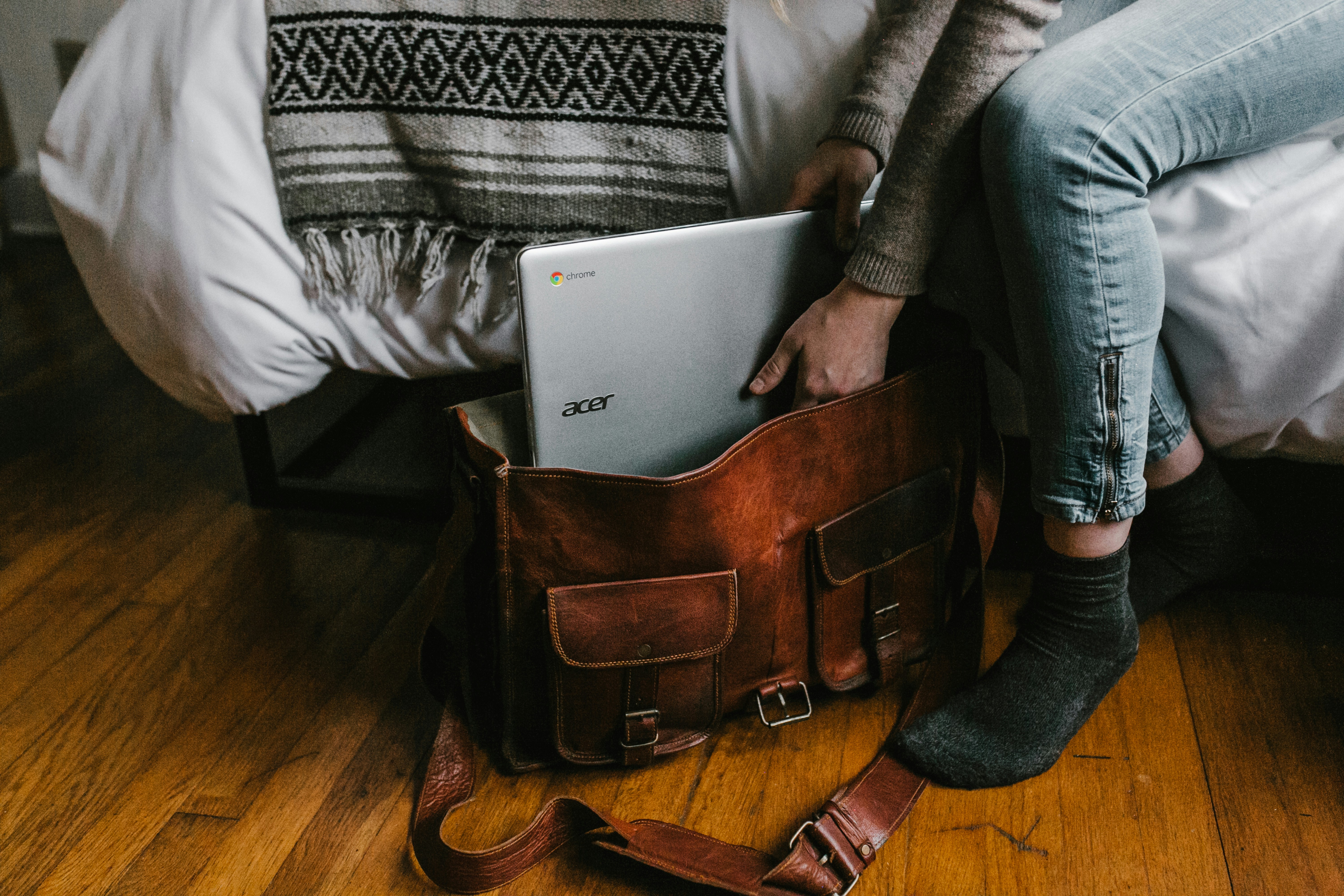 A person is placing their laptop into a leather stachel on the floor.