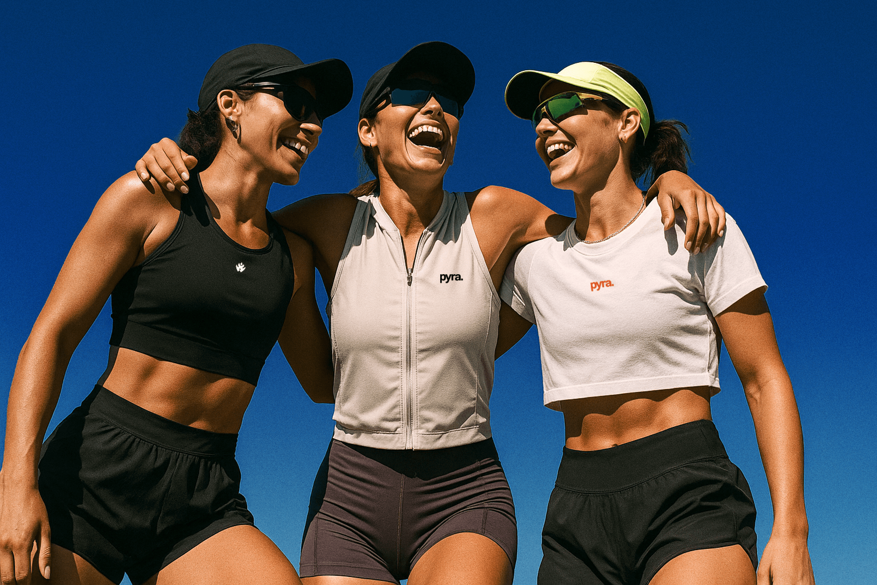 Three women in athletic wear smiling and linking arms outdoors under a bright blue sky, each wearing Pyra-branded sports apparel and visors or caps.