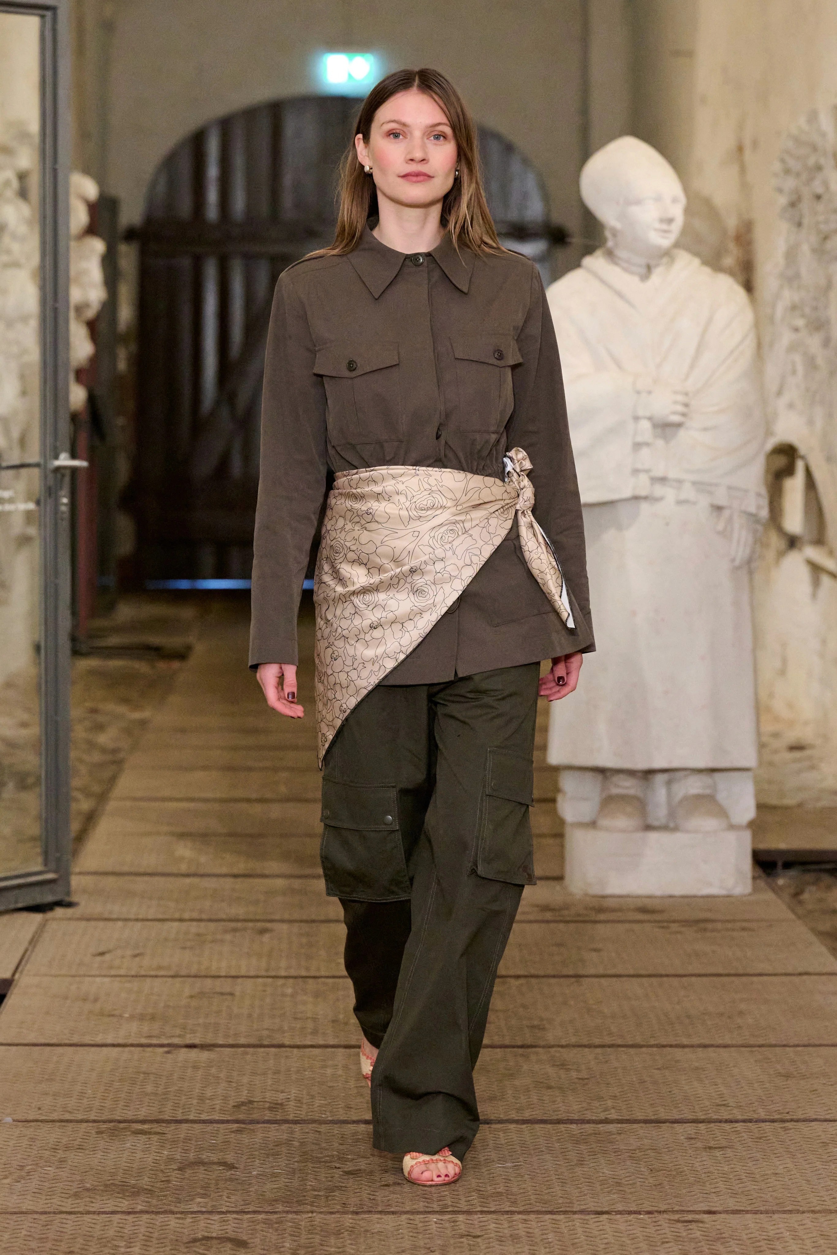 Une mannequin au défilé Operasport porte une chemise militaire, un foualrd en jupe beige et un pantalon cargo vert foncé