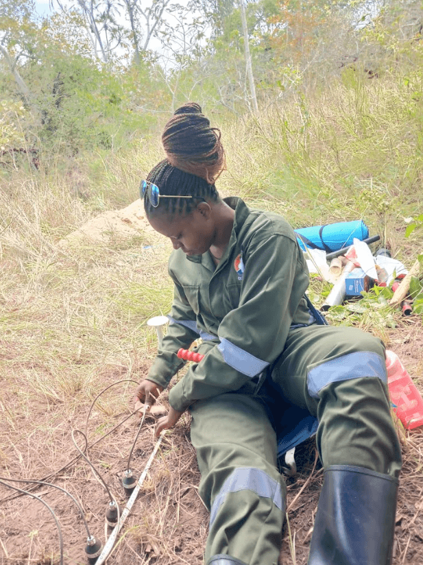 Lady in green overalls in a field doing an experiement
