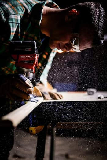 Carpenter Using power tool to shape wood while wearing safety goggles and gloves in workshop.