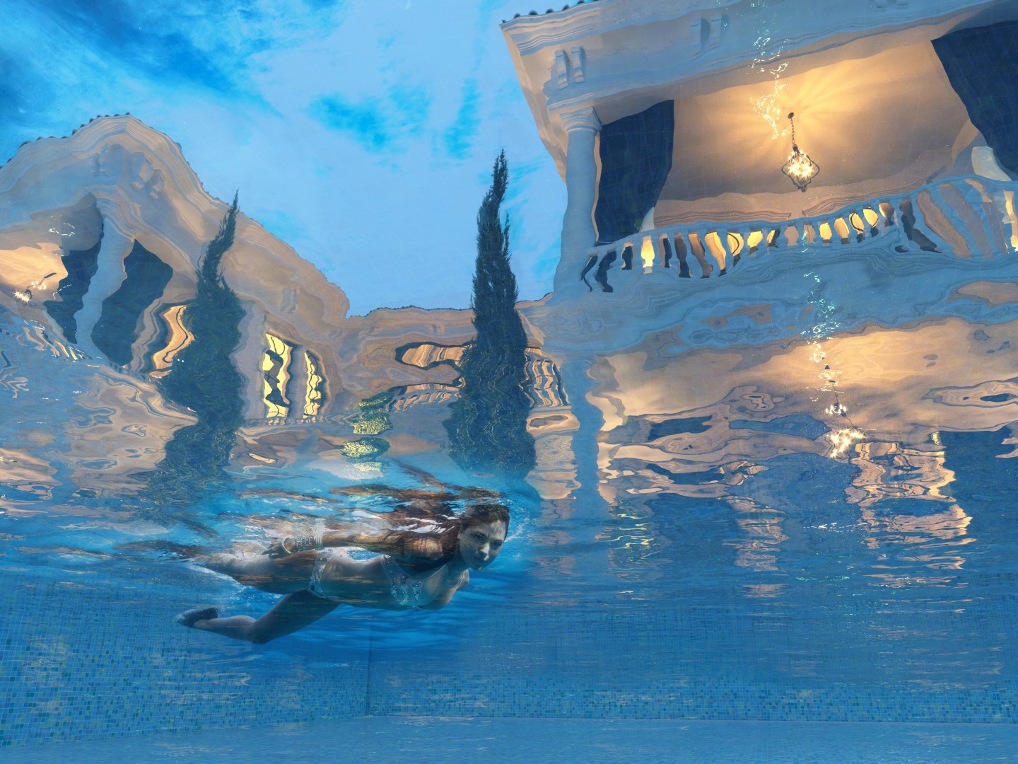 A person swims underwater in a luxurious pool, reflecting an opulent mansion with ornate balconies and glowing chandeliers, set against a clear blue sky.